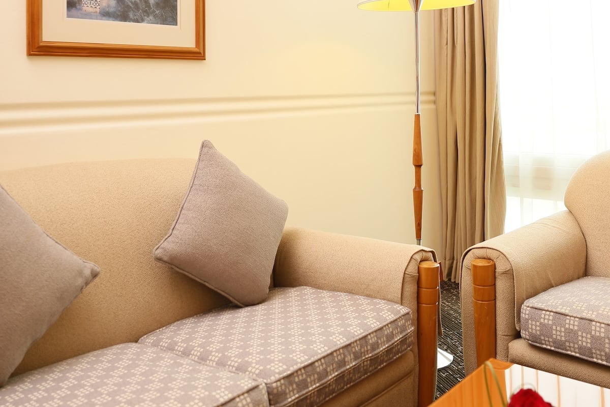 A hotel room with a sofa, a table with a vase of flowers, a lamp, and a framed picture on the wall.