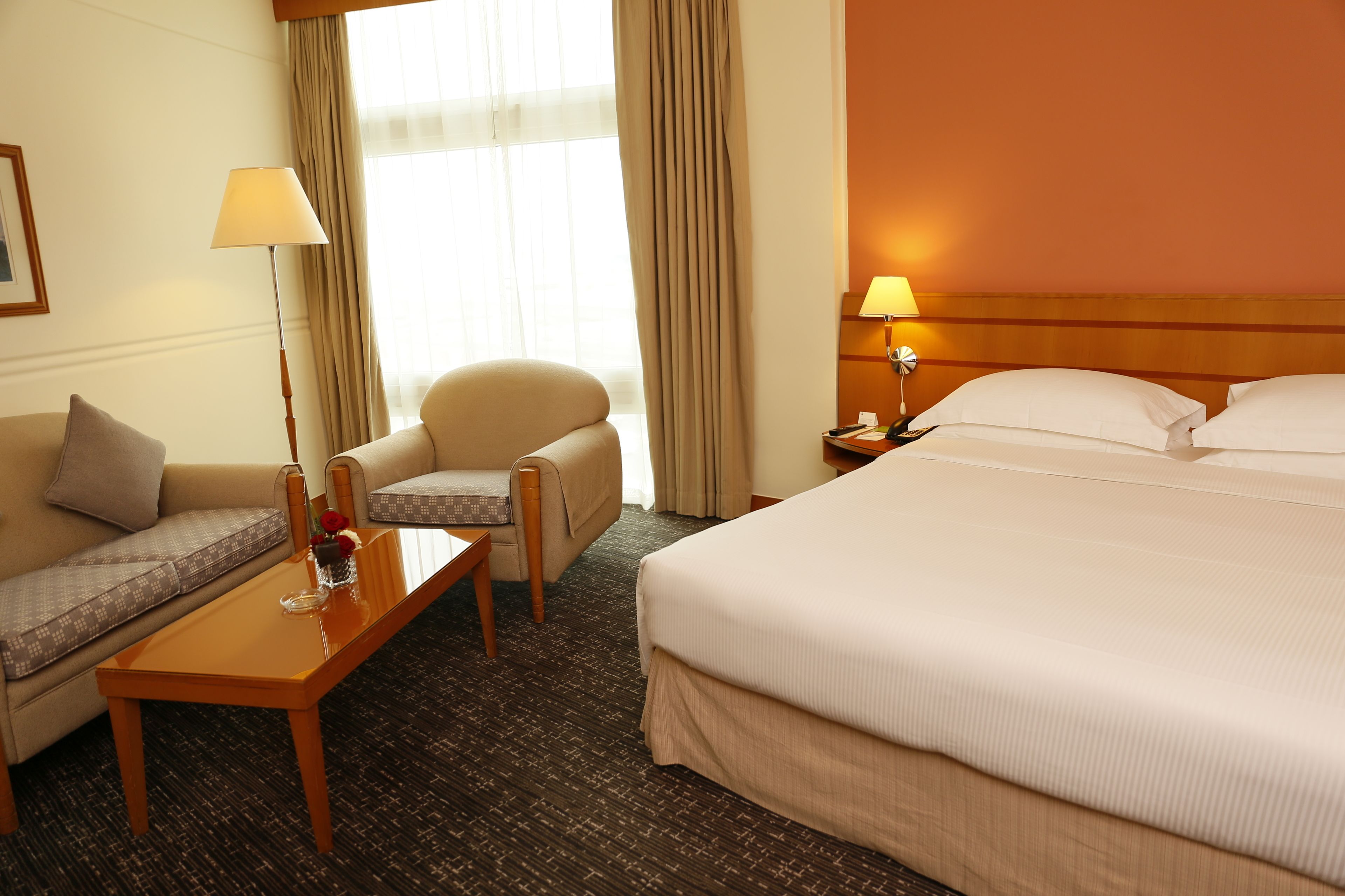 A hotel room with a bed, a sofa, a chair, a table, and a lamp.
