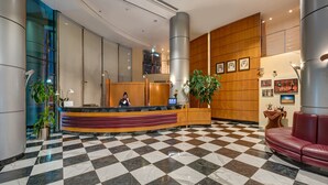 A hotel lobby with a checkered floor, a reception desk, a large plant, and a red leather couch. - J5 Hotels - Port Saeed (Dubai)