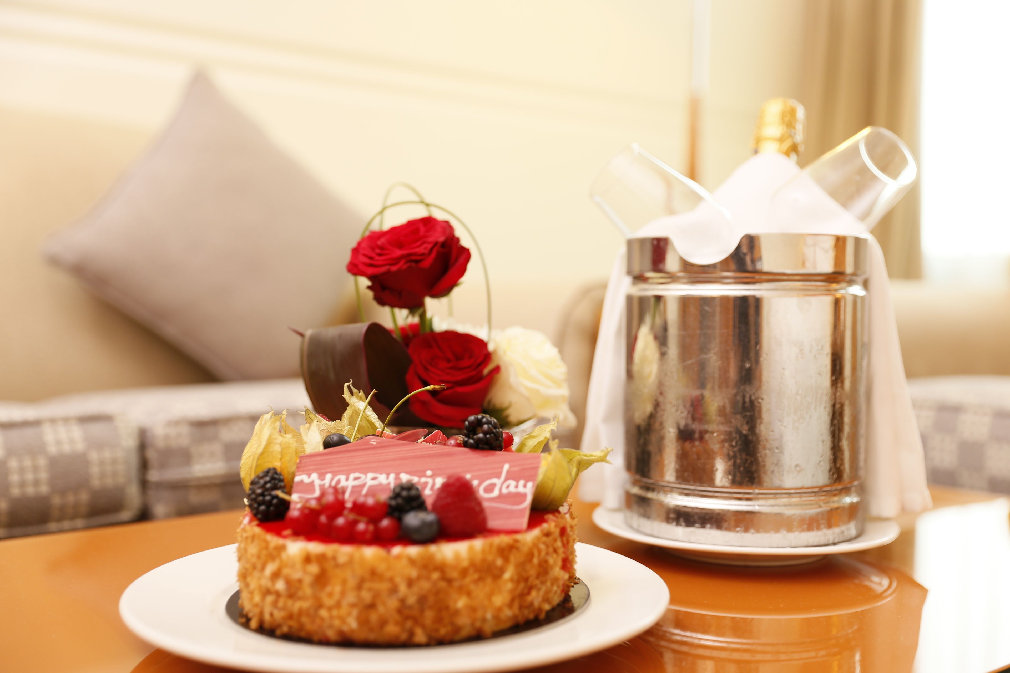 A dessert with a "Happy Birthday" sign, a silver pitcher, and a red rose on a table.