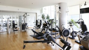 A gym with various exercise equipment, large windows, and a wooden floor. - J5 Hotels - Port Saeed (Dubai)
