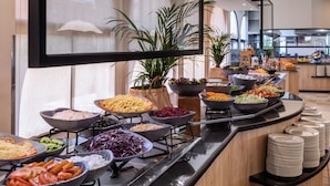 Un bufé con diversos alimentos y una pila de platos a la derecha.