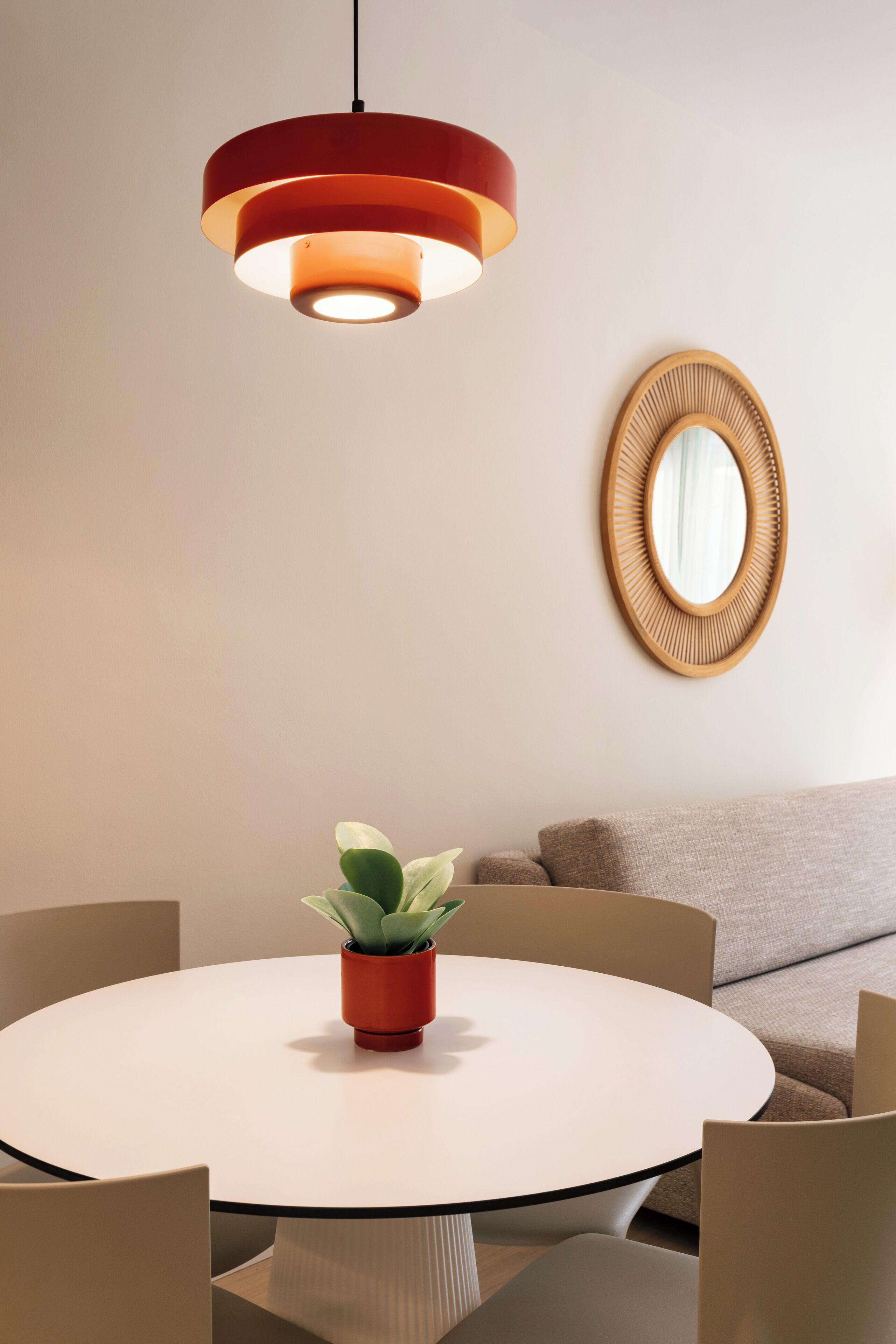 Ein runder Esstisch mit einem Blumentopf, umgeben von Stühlen, unter einer modernen Pendelleuchte.