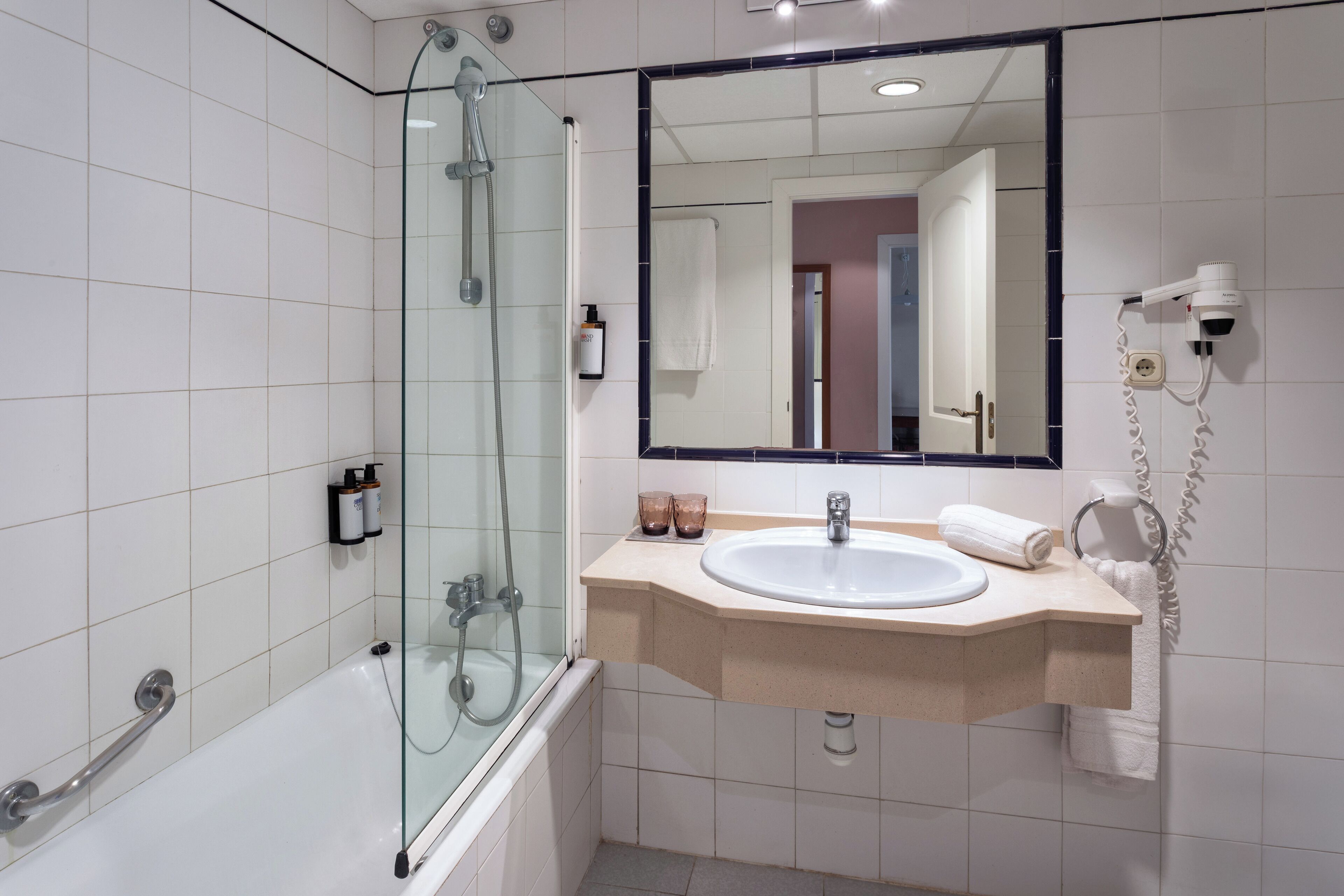 Een moderne badkamer met een douche in glazen cabine, een witte wastafel en een spiegel erboven.
