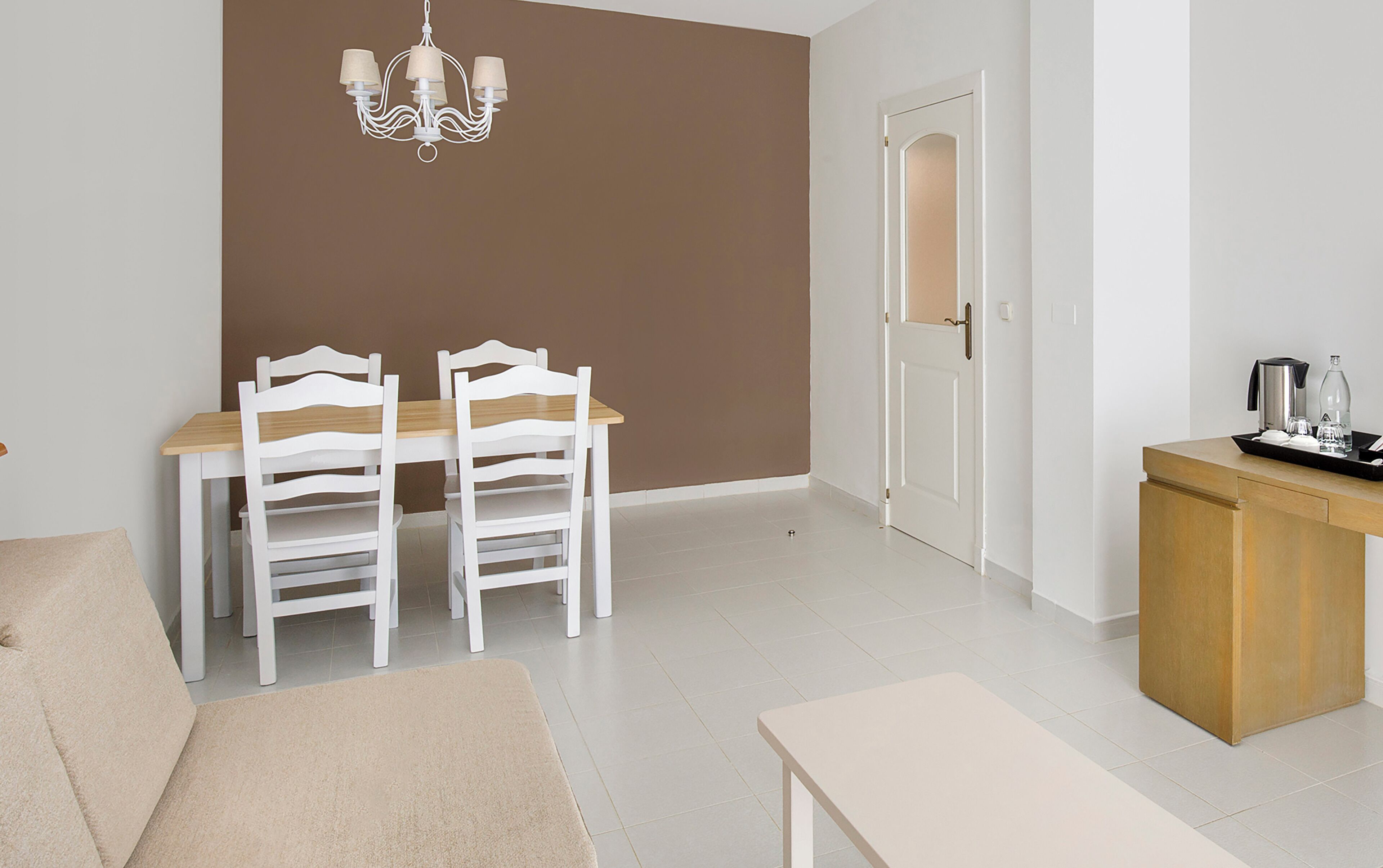 Habitación moderna y minimalista con comedor que incluye una mesa y sillas blancas, un mueble de madera con una bandeja de objetos y una puerta que da a otra habitación.