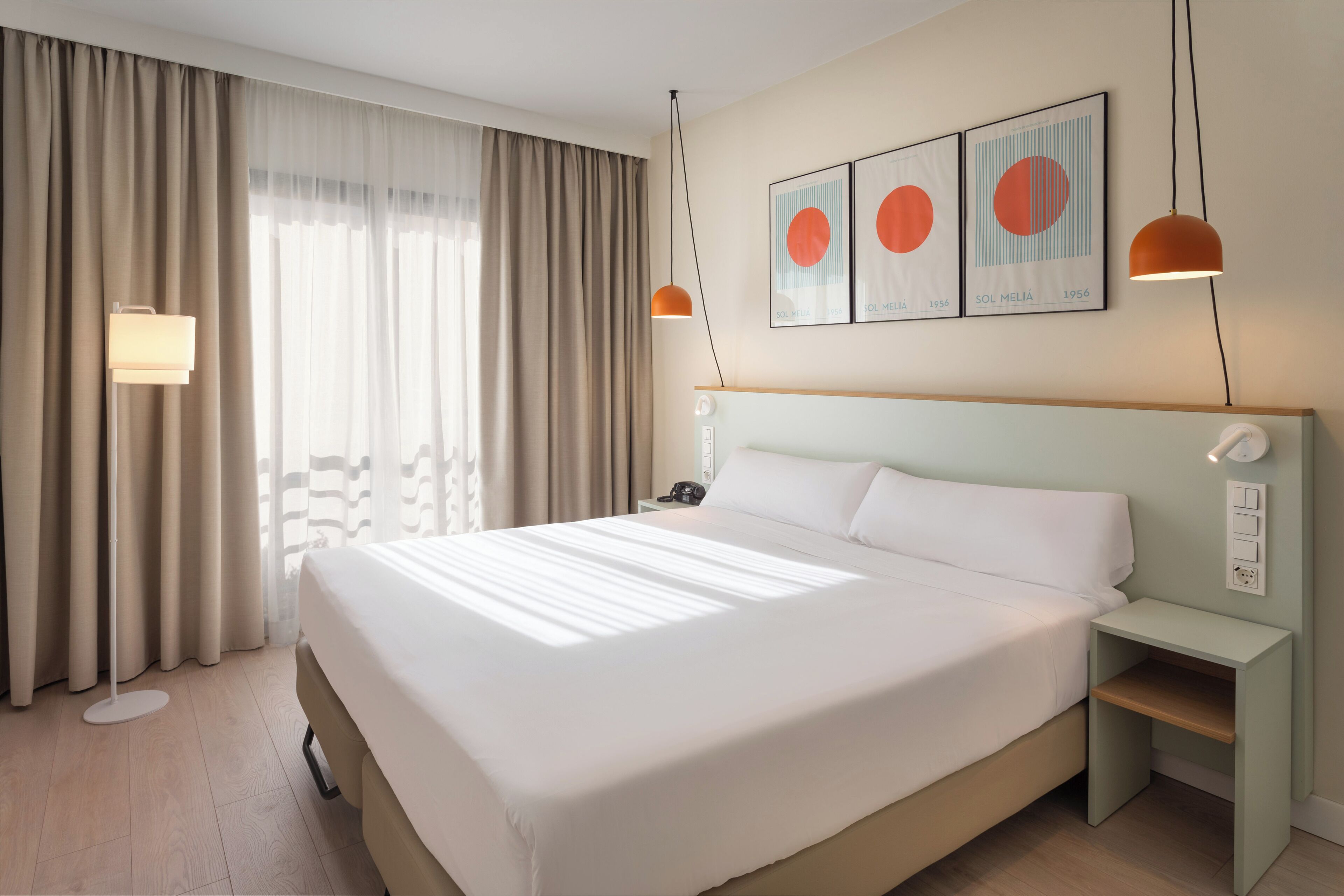 Ein modernes Hotelzimmer mit einem großen Bett, einem Nachttisch, Vorhängen und einem Fenster.