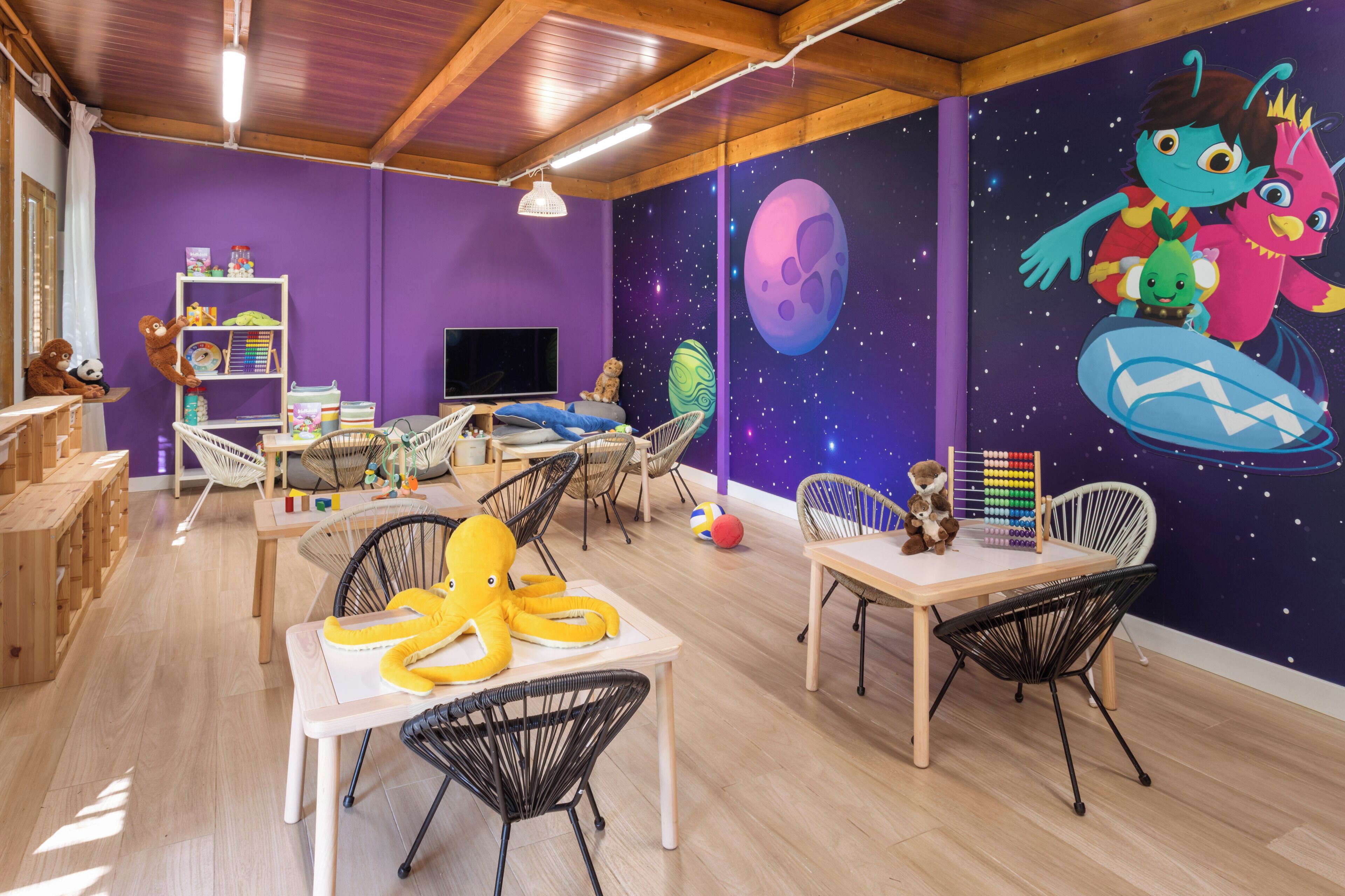 A children's playroom with a starry wall mural, wooden furniture, and a variety of toys and educational materials.