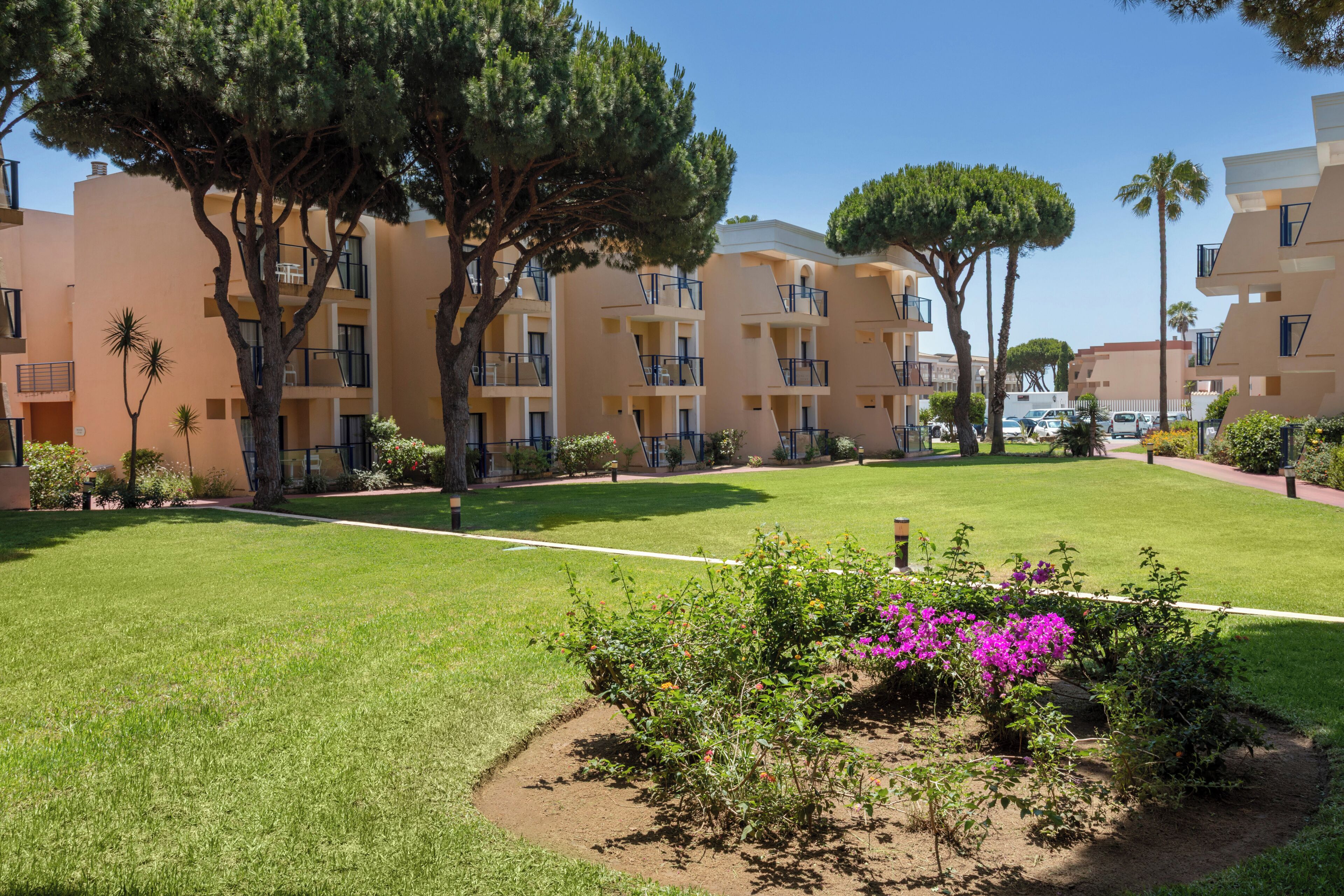 A courtyard with a lawn, trees, and a building with balconies.