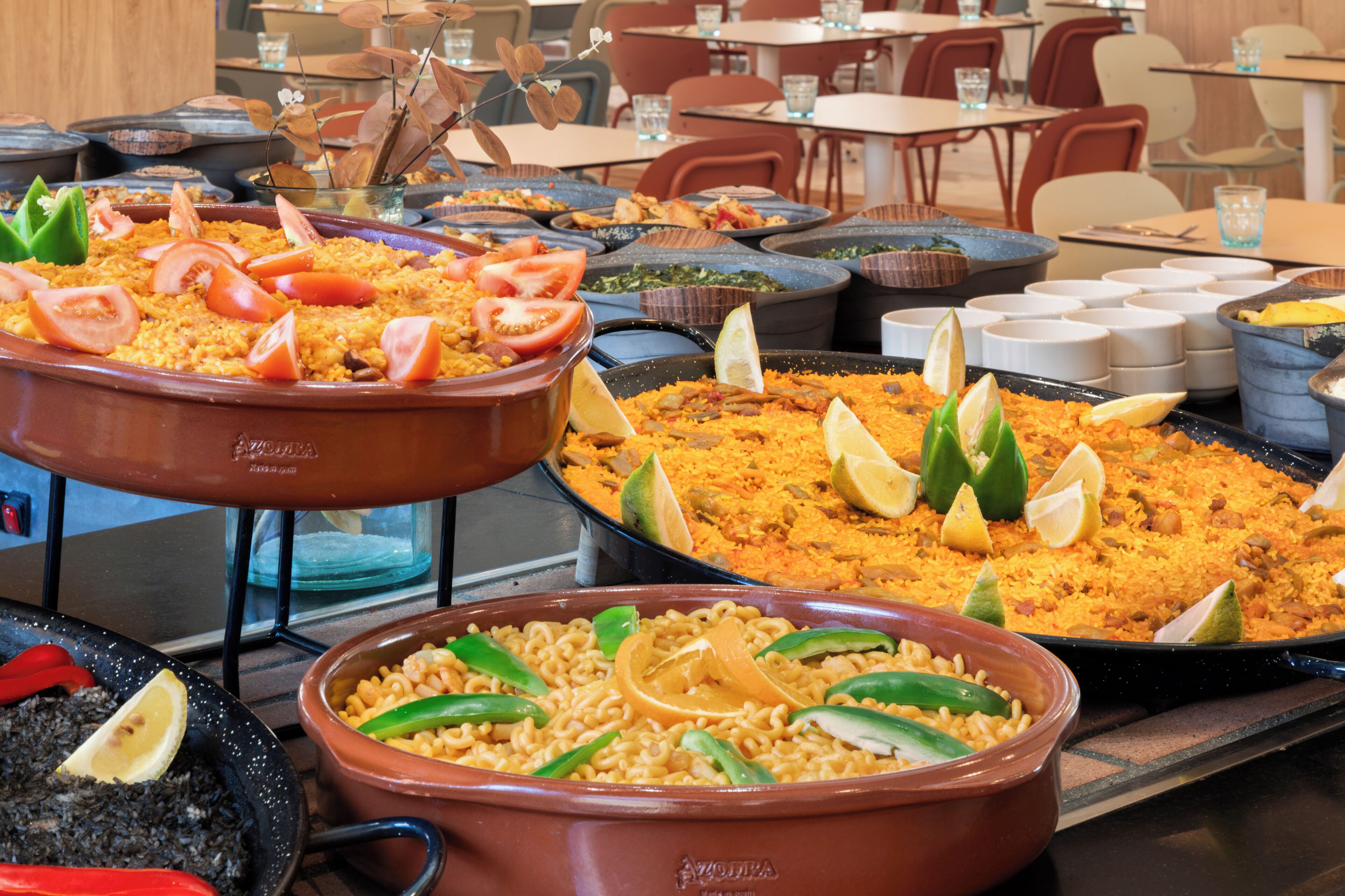 A buffet with various dishes, including rice and pasta, in large serving pots.