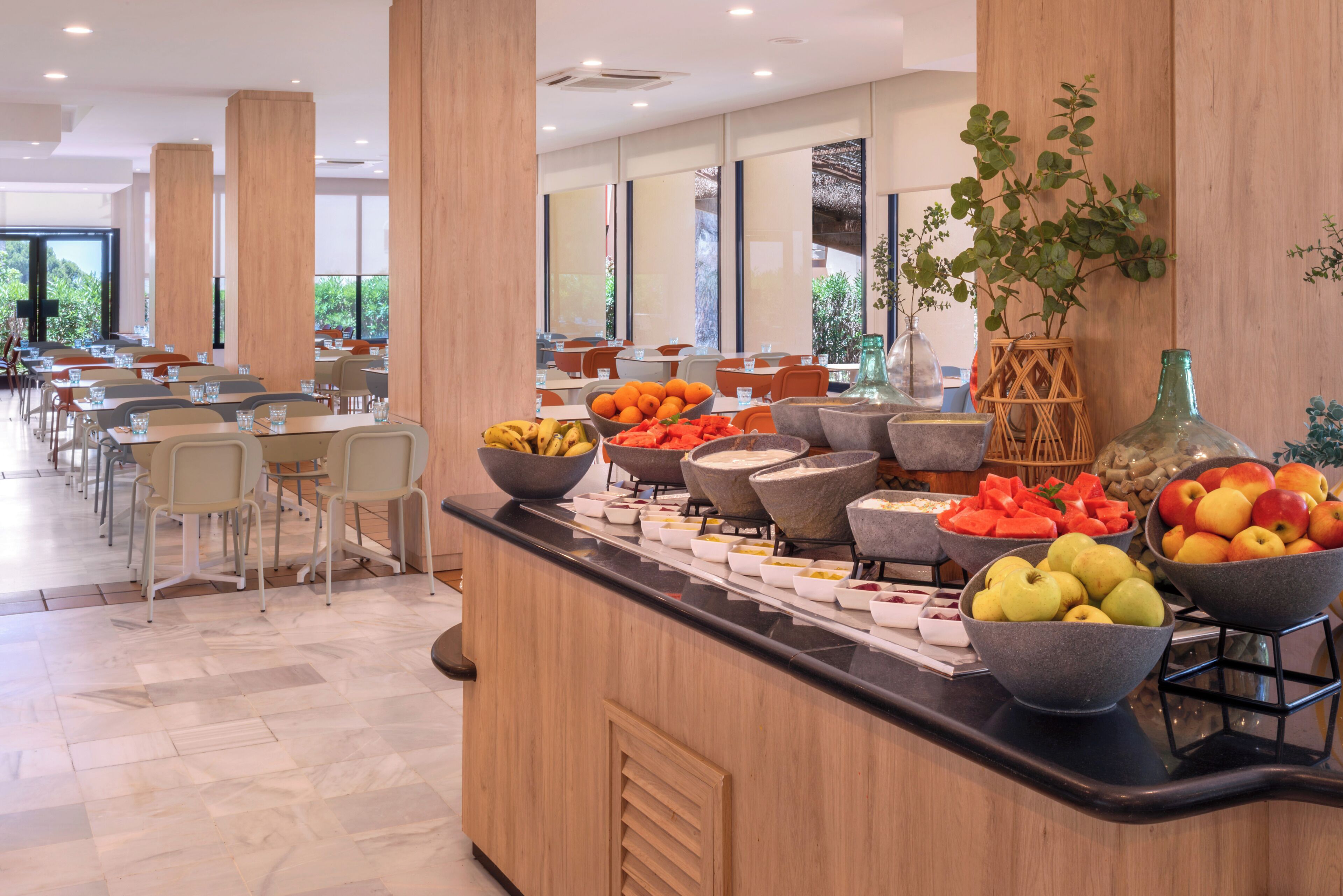 A buffet area with various fruits and bowls of food, wooden pillars, and a view of the outdoors.