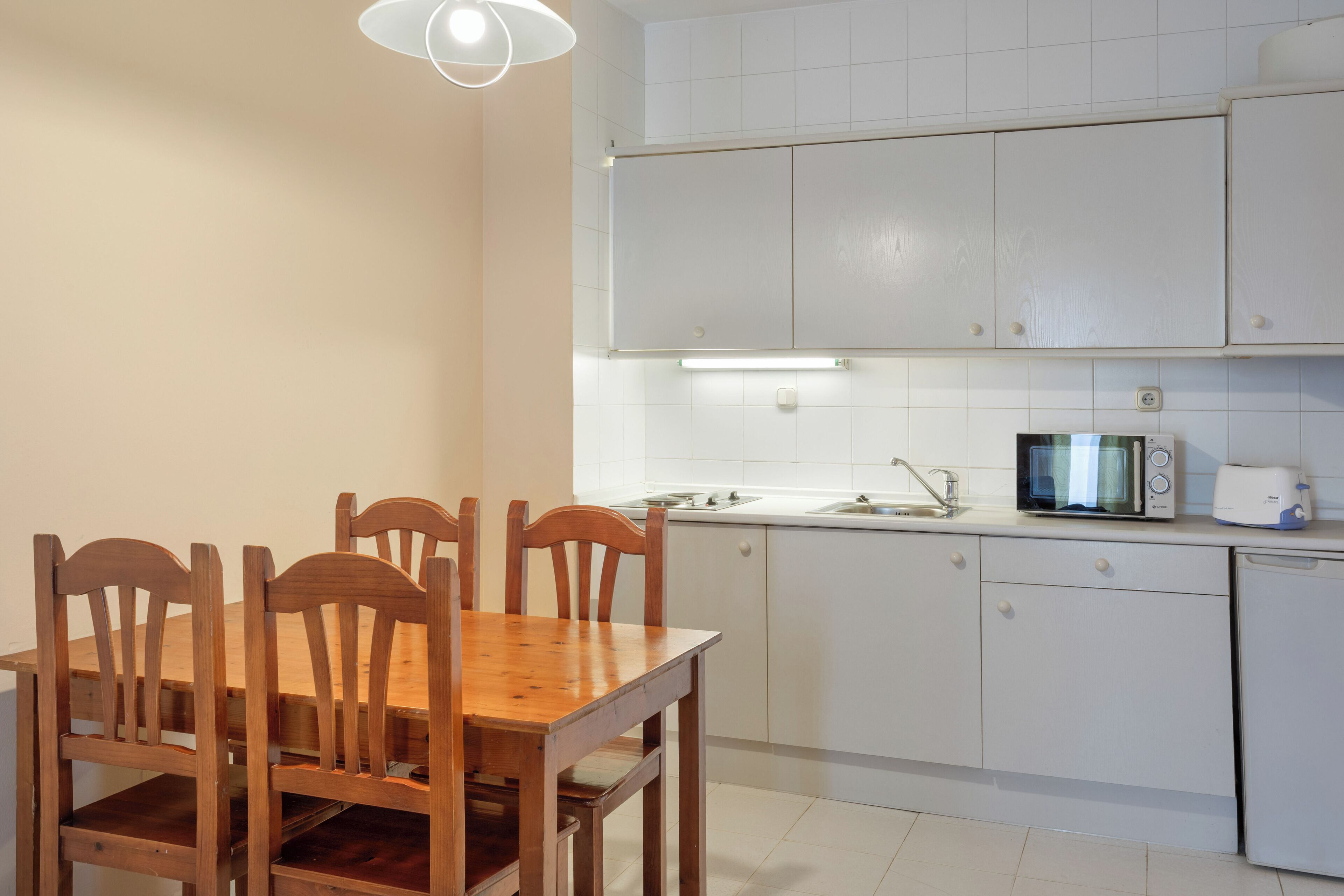 A kitchen with white cabinets, a wooden dining table with chairs, a microwave, and a toaster.