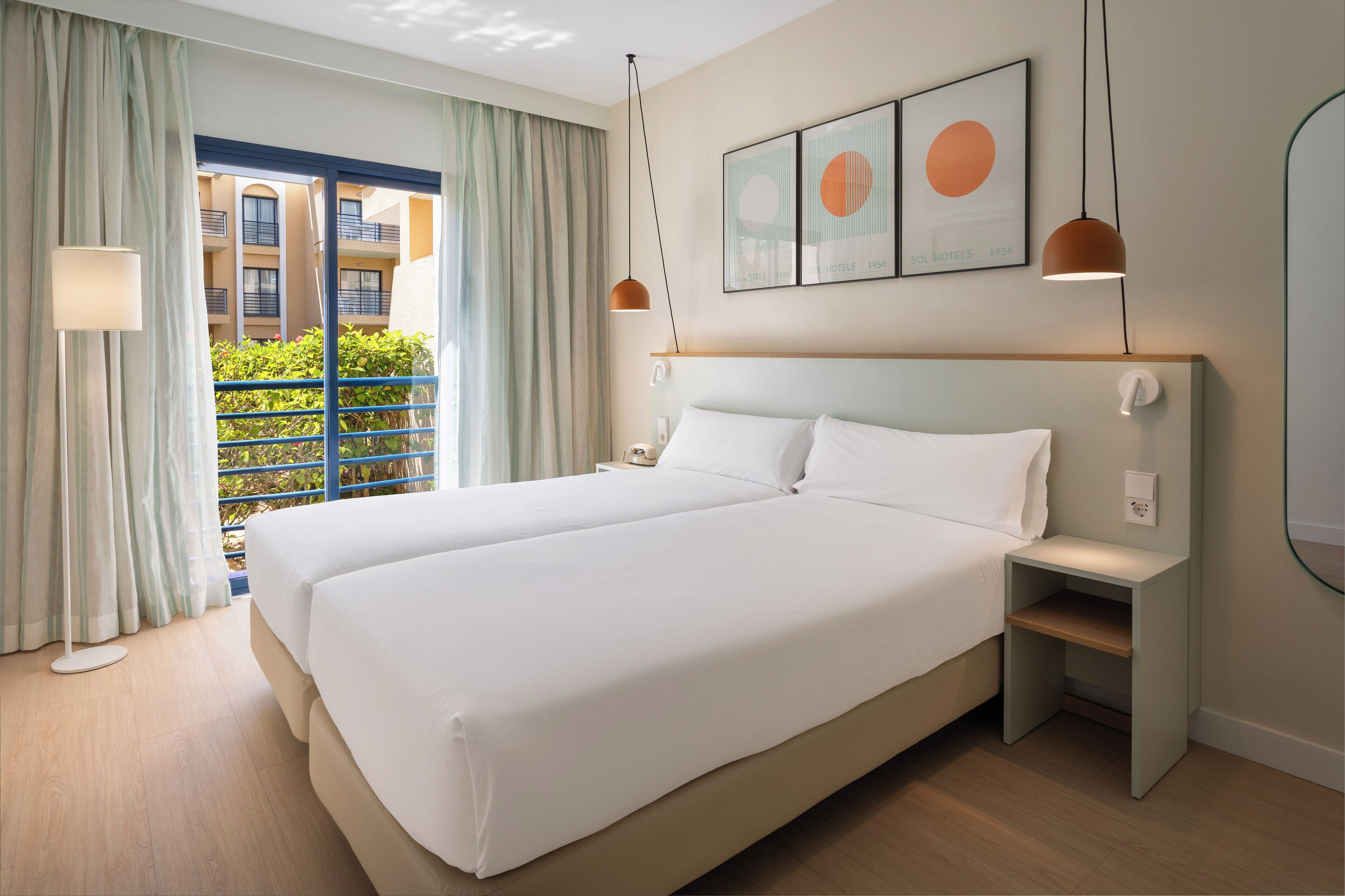 Une chambre d’hôtel avec un grand lit, une table de chevet, une lampe et une vue sur le balcon extérieur.