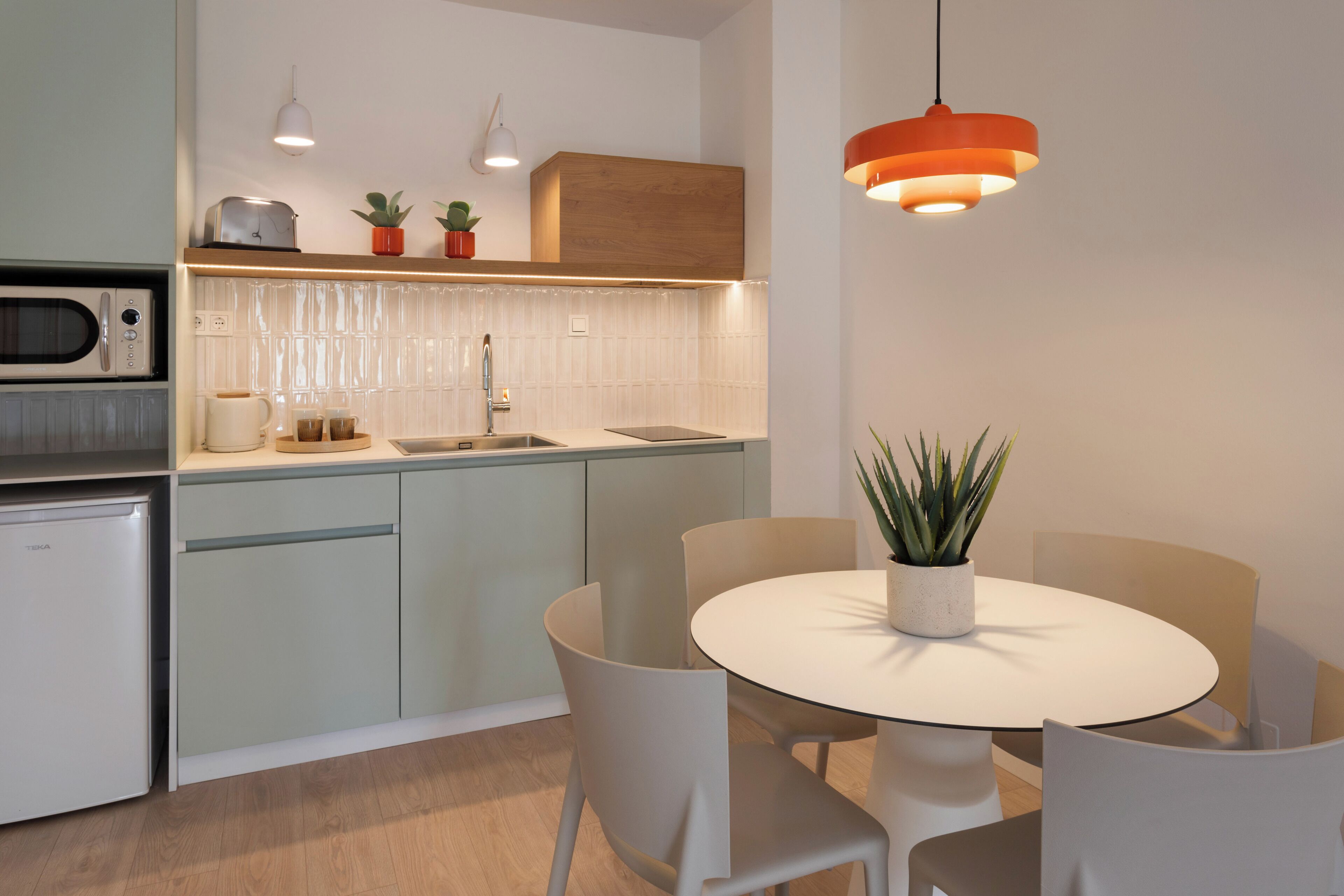 Een moderne keuken met een inbouwoven, een spoelbak en een eethoek met een ronde tafel en stoelen.