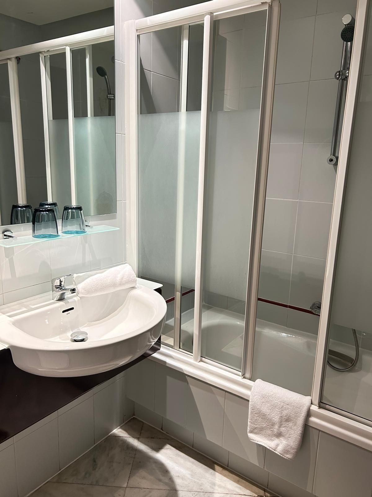 Ein modernes Badezimmer mit einer gläsernen Duschkabine, einem weißen Waschbecken und einem Spiegel.