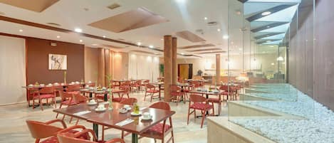 A spacious dining area with multiple tables and chairs, a large glass wall, and a pebbled walkway.