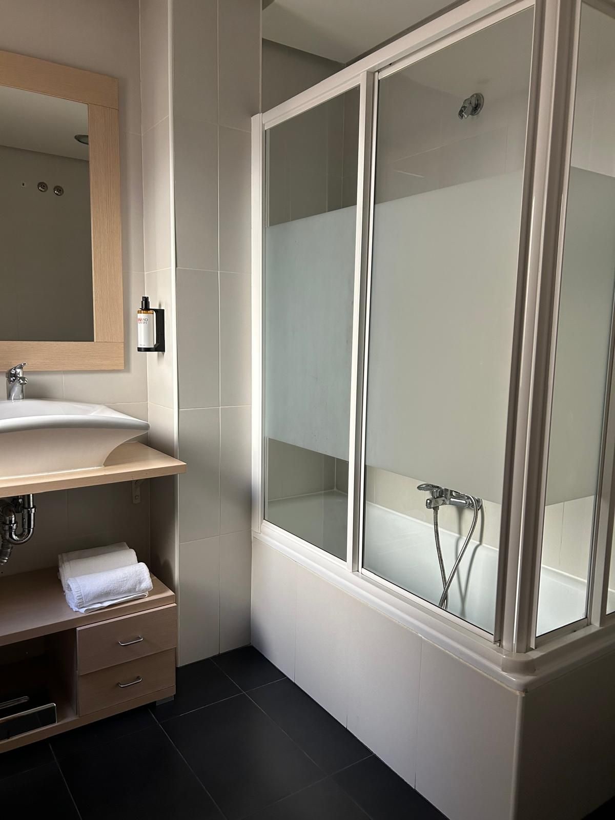 Un baño moderno con ducha envuelta en vidrio, tocador de madera con espejo y un perchero para toallas.