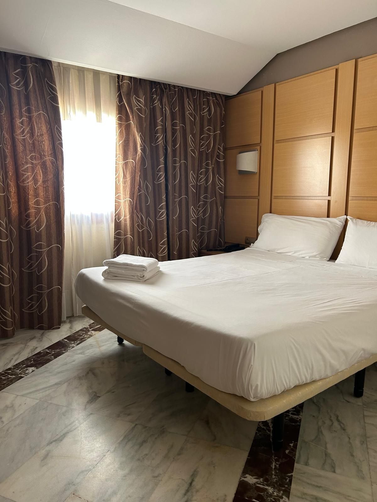 A hotel room with a large bed, wooden headboard, and a marble floor.