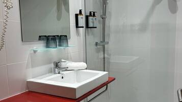 Un baño moderno con ducha de vidrio, un lavabo blanco con encimera roja y un espejo sobre el lavabo.