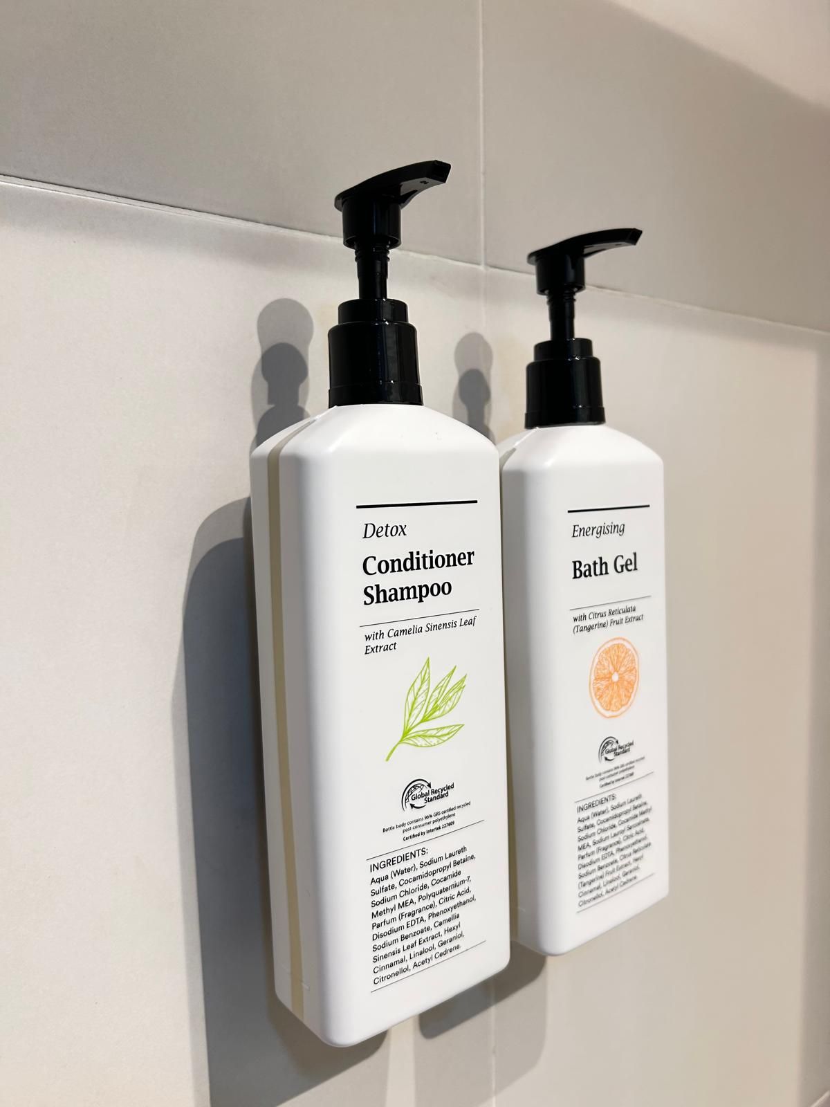 Dos botellas de champú y gel de baño sobre una pared blanca.