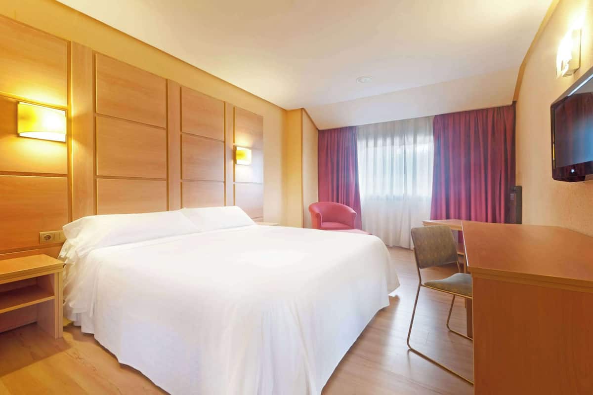 Una habitació d'hotel amb un llit gran, una taula de treball, una cadira i una televisió.