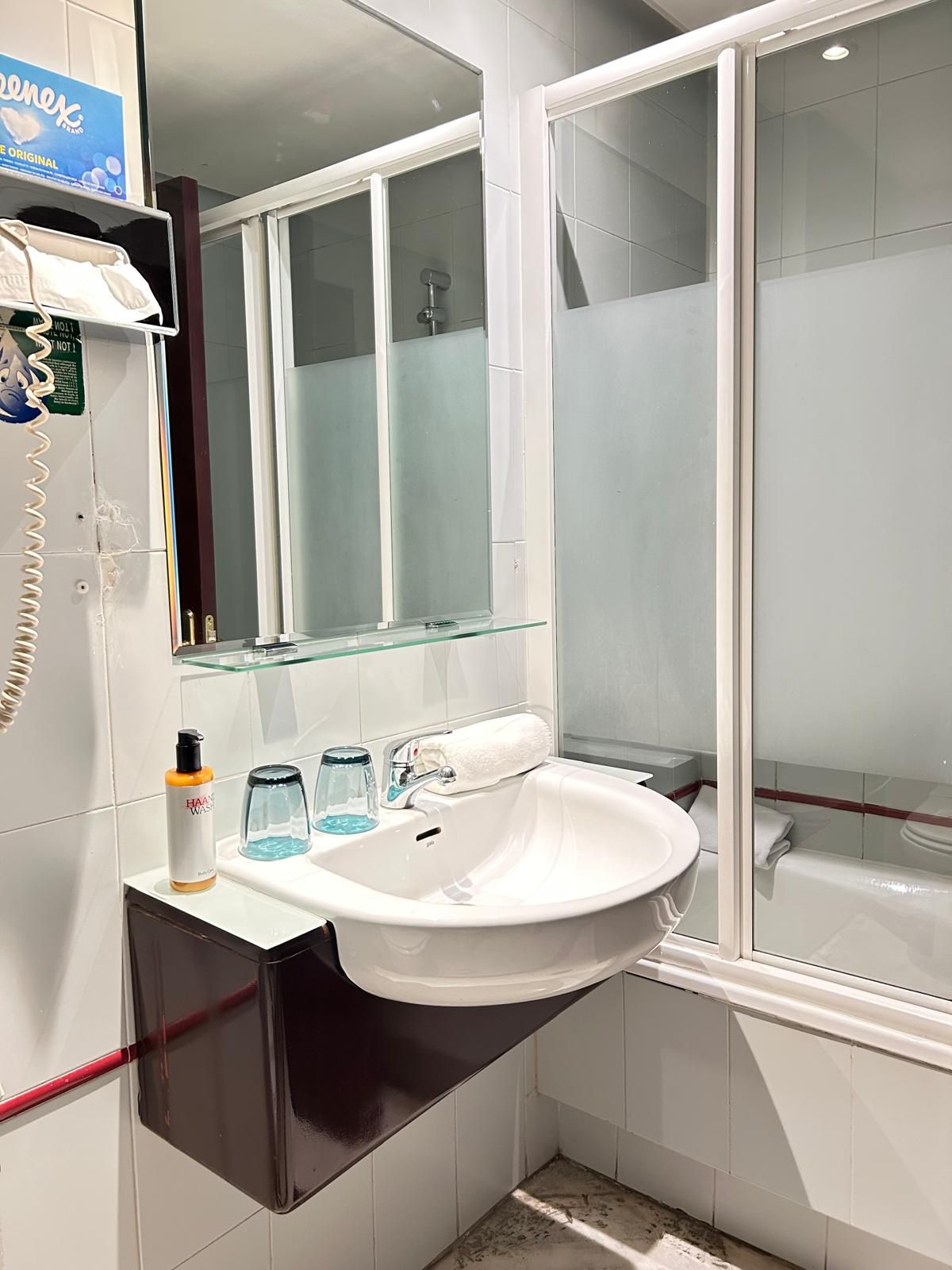 Un baño con lavamanos blanco, cabina de ducha de vidrio y espejo sobre el lavamanos.