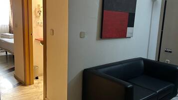 Habitación de hotel con sofá de cuero negro, un cuadro en la pared y suelo de baldosas.