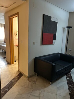 A hotel room with a black leather sofa, a painting on the wall, and a tiled floor. - Hotel Puertollano 3* by eme hoteles (Puertollano)