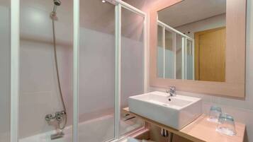 Un baño moderno con ducha envuelta en vidrio, un lavabo blanco y un mueble de tocador de madera.