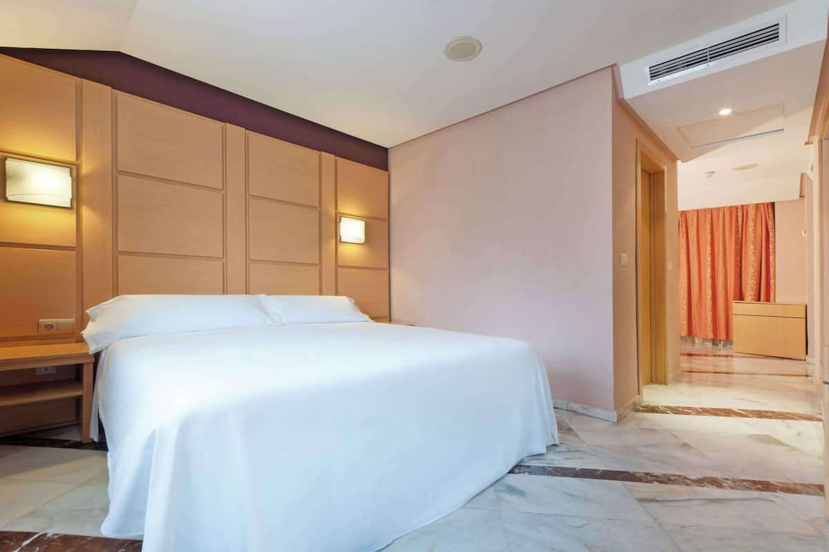 Habitació d'hotel amb un llit gran, parets de fusta i un terra de marbre.