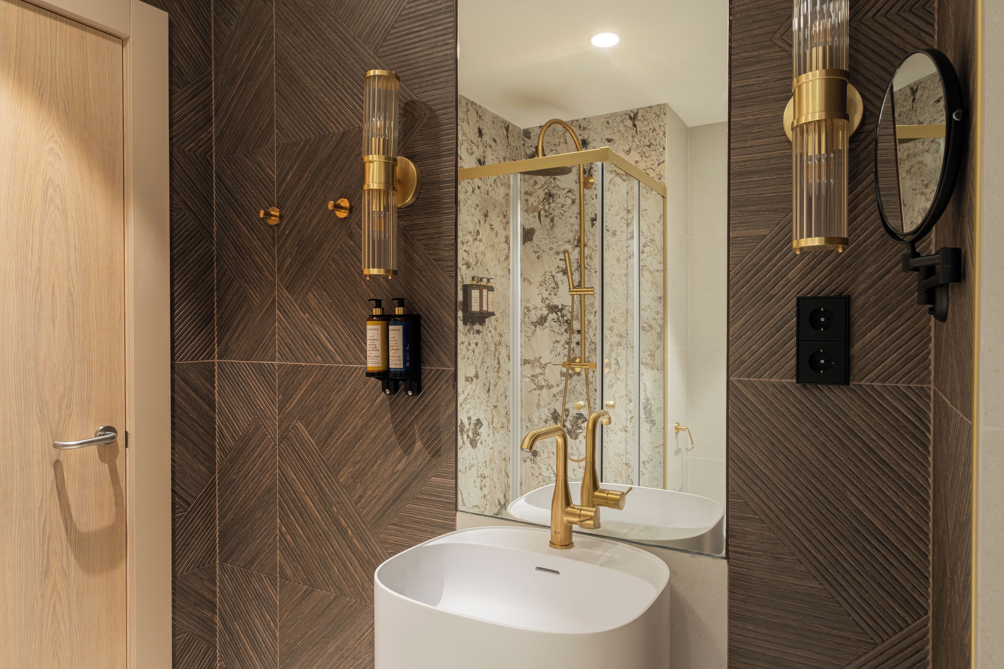 Un baño moderno con un lavamanos blanco, detalles dorados y un espejo grande.
