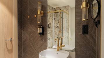 Un baño moderno con un lavamanos blanco, detalles dorados y un espejo grande.