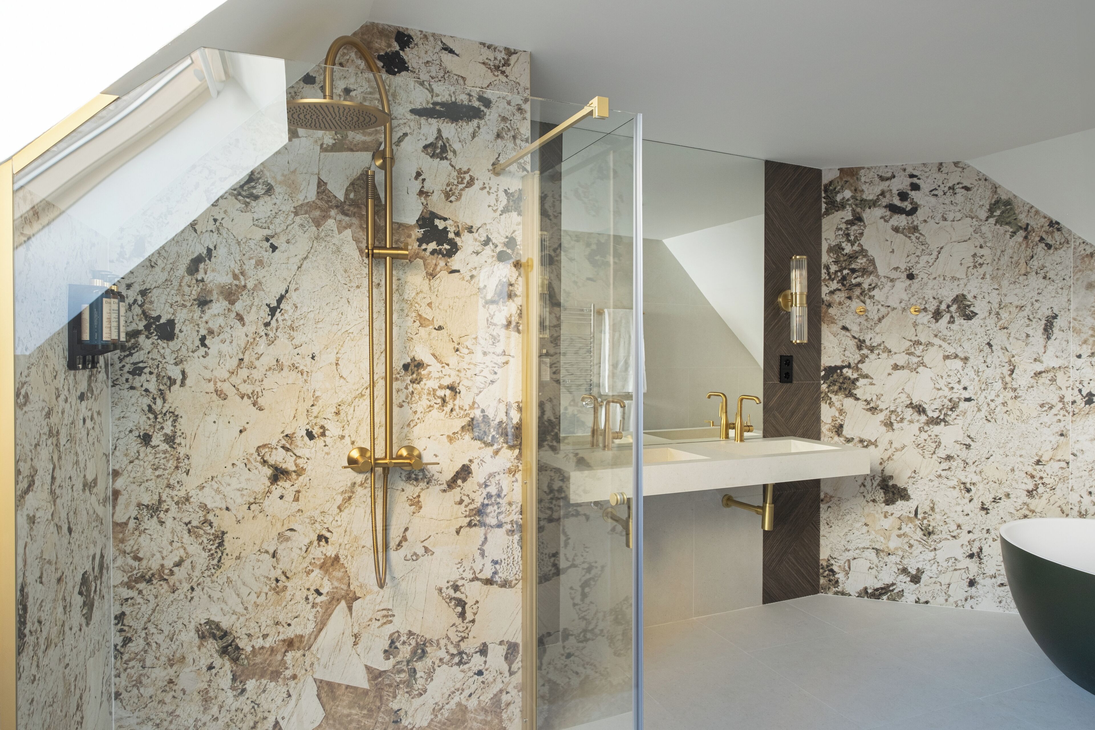 A modern bathroom with a glass-enclosed shower, a white sink, and a marble wall.