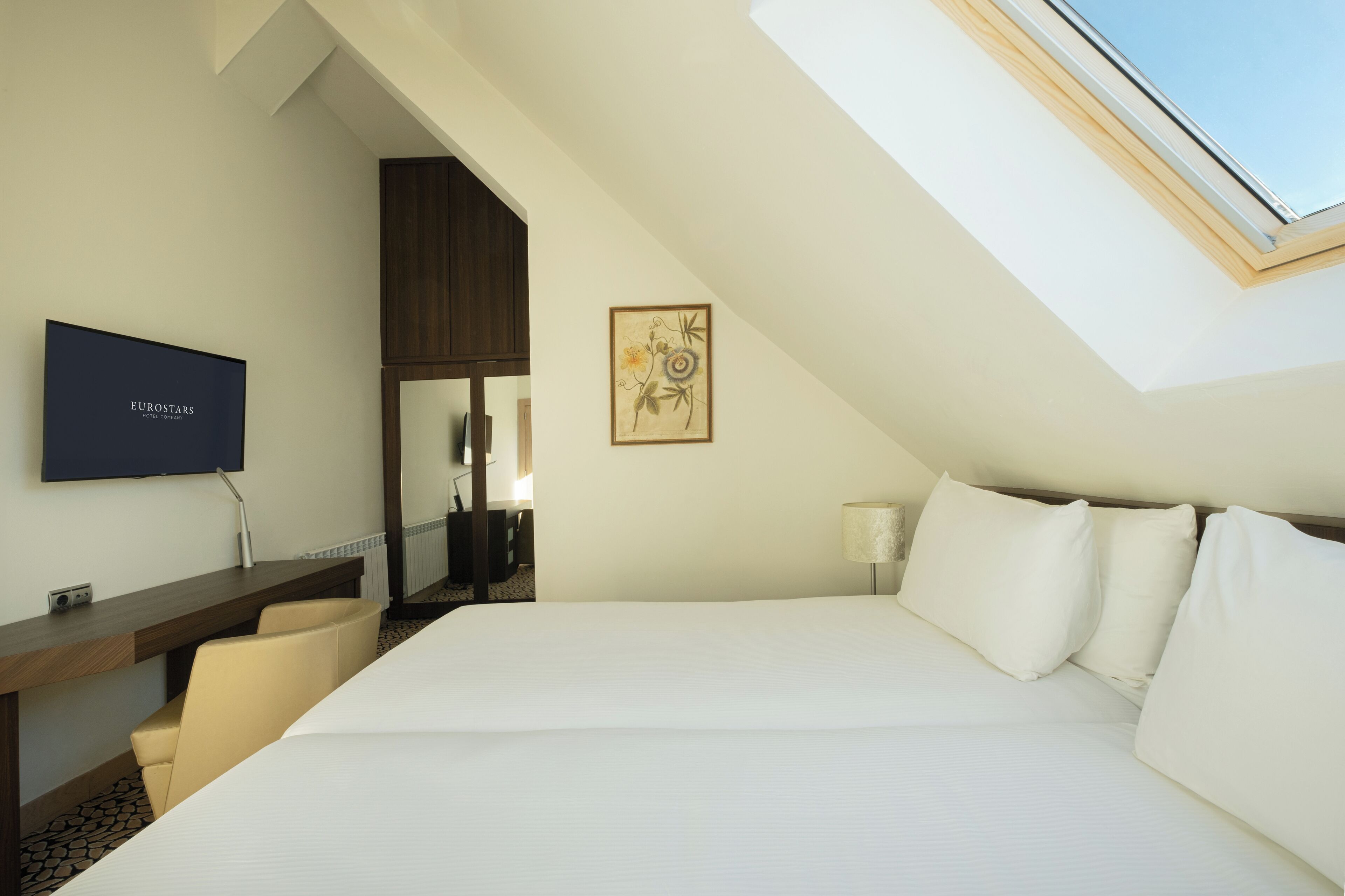 Een hotelkamer met een groot bed, een bureau met stoel, een televisie en een dakraam.