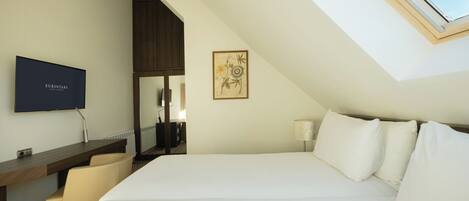 Een hotelkamer met een groot bed, een bureau met stoel, een televisie en een dakraam.