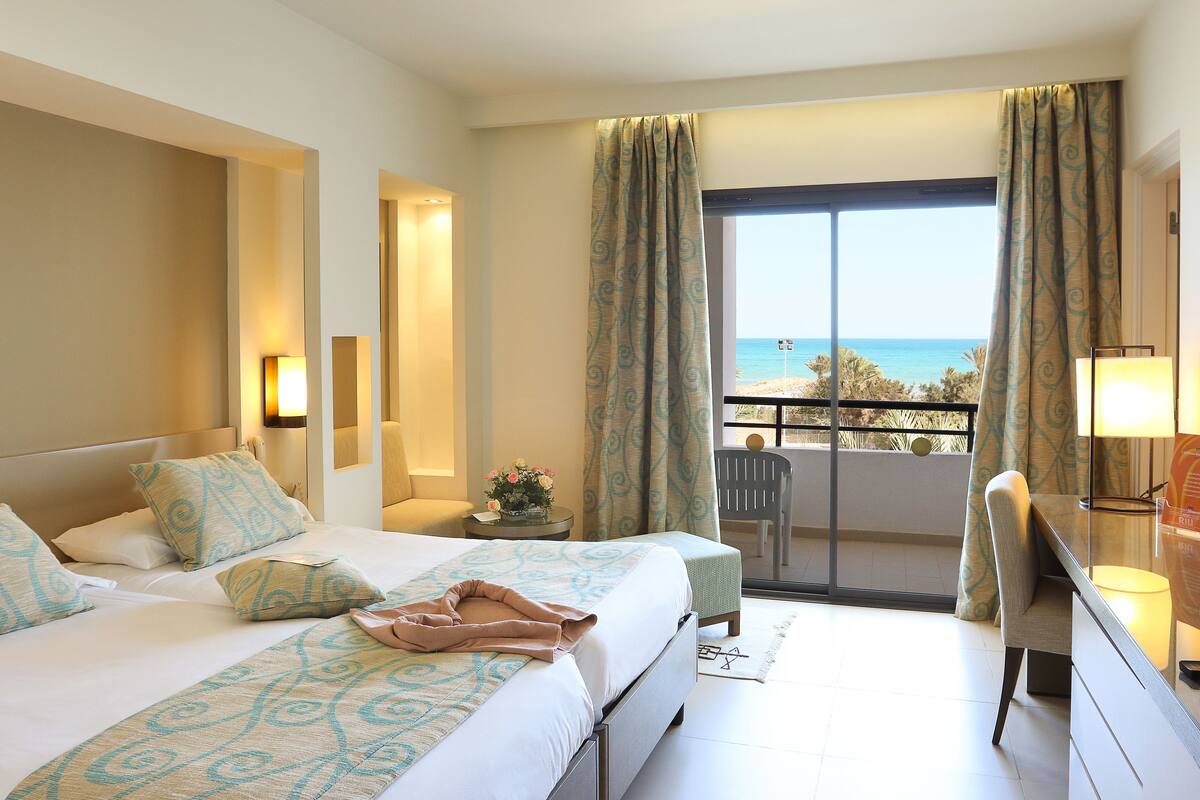 A hotel room with a large bed, a desk, and a view of the sea.