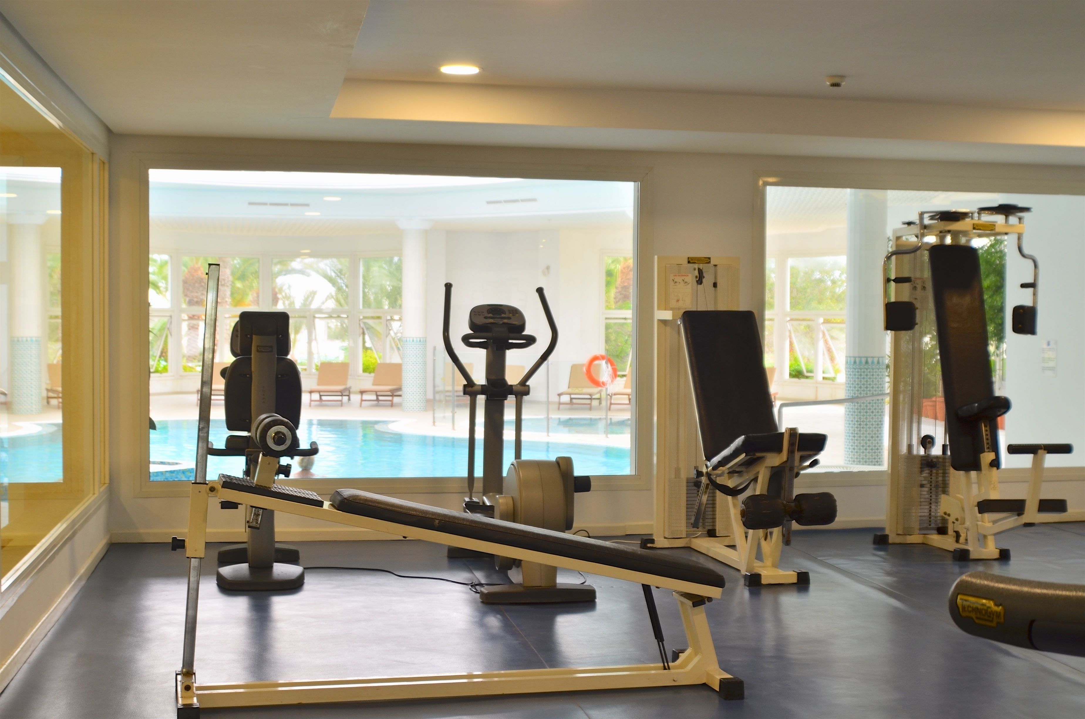 Ein Fitnessraum mit Trainingsgeräten, einem Pool und großen Fenstern.