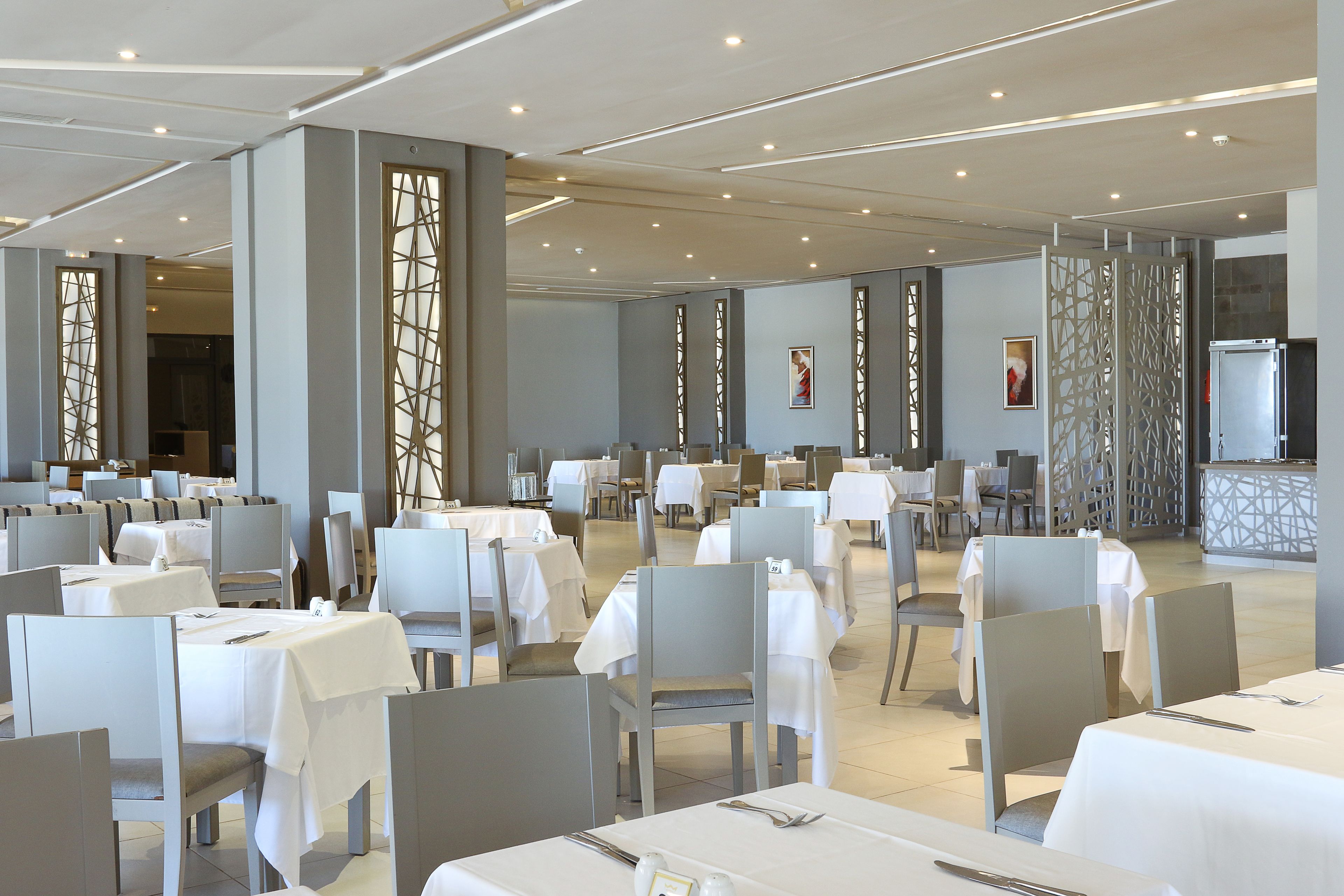 A spacious dining area with multiple tables and chairs, high ceilings with recessed lighting, and decorative panels.