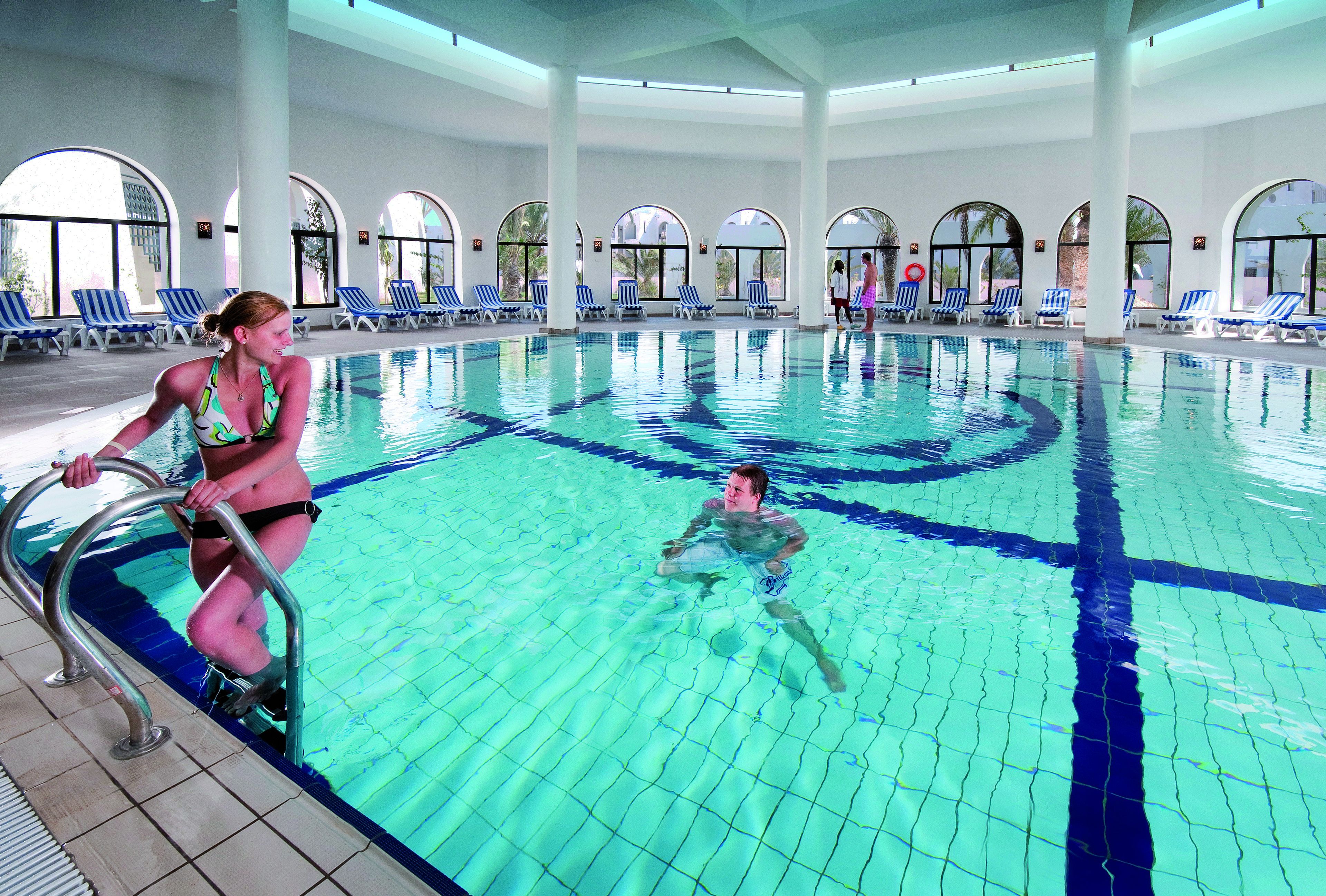 A swimming pool with clear blue water, a diving board, and lounge chairs along the poolside.