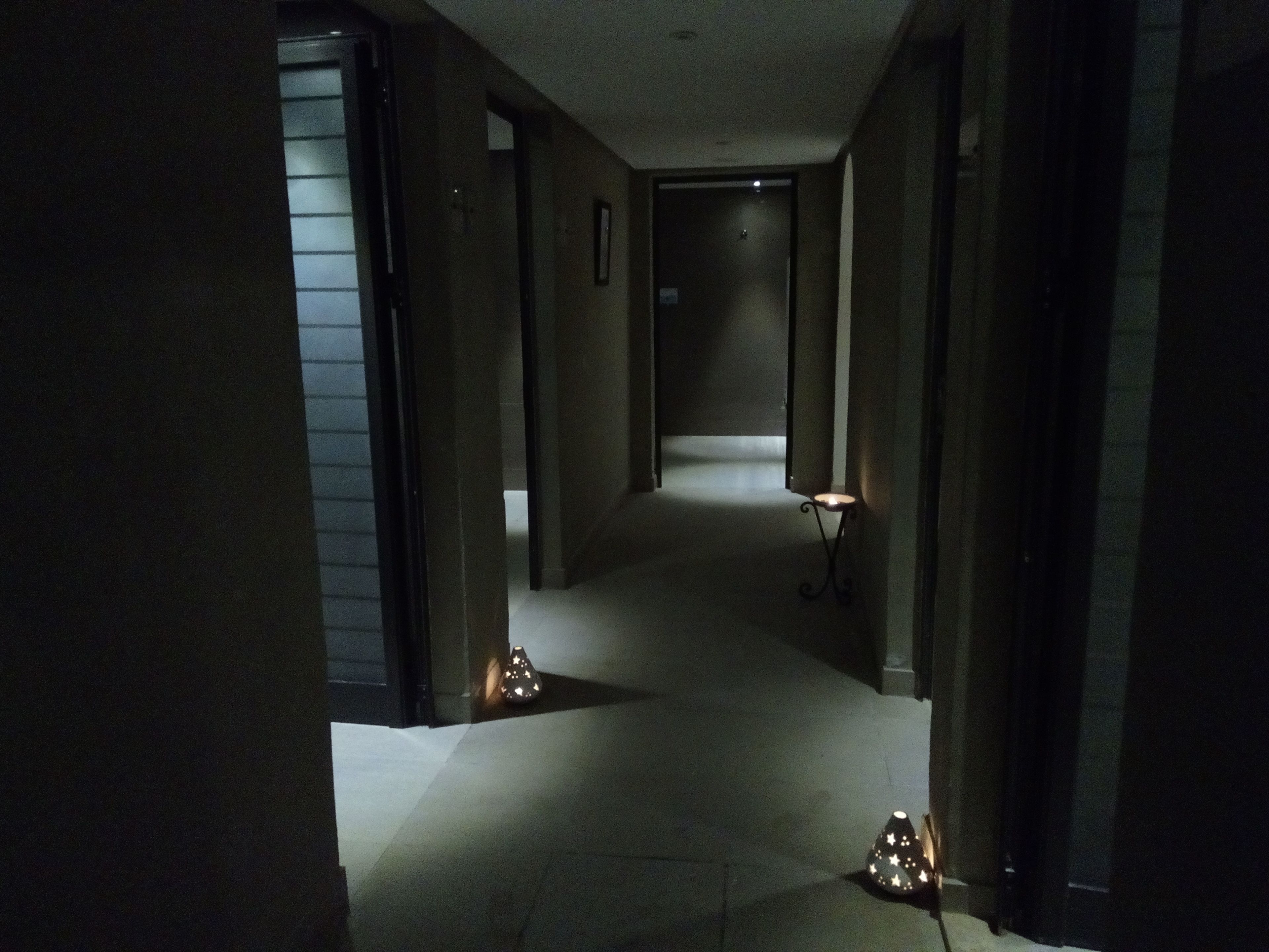 Un pasillo tenuemente iluminado con suelo alfombrado, que conduce a una puerta al final. Hay dos pequeñas lámparas en forma de estrella en el camino.