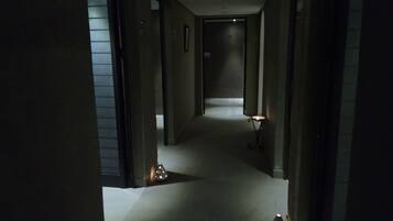 Un pasillo tenuemente iluminado con suelo alfombrado, que conduce a una puerta al final. Hay dos pequeñas lámparas en forma de estrella en el camino.