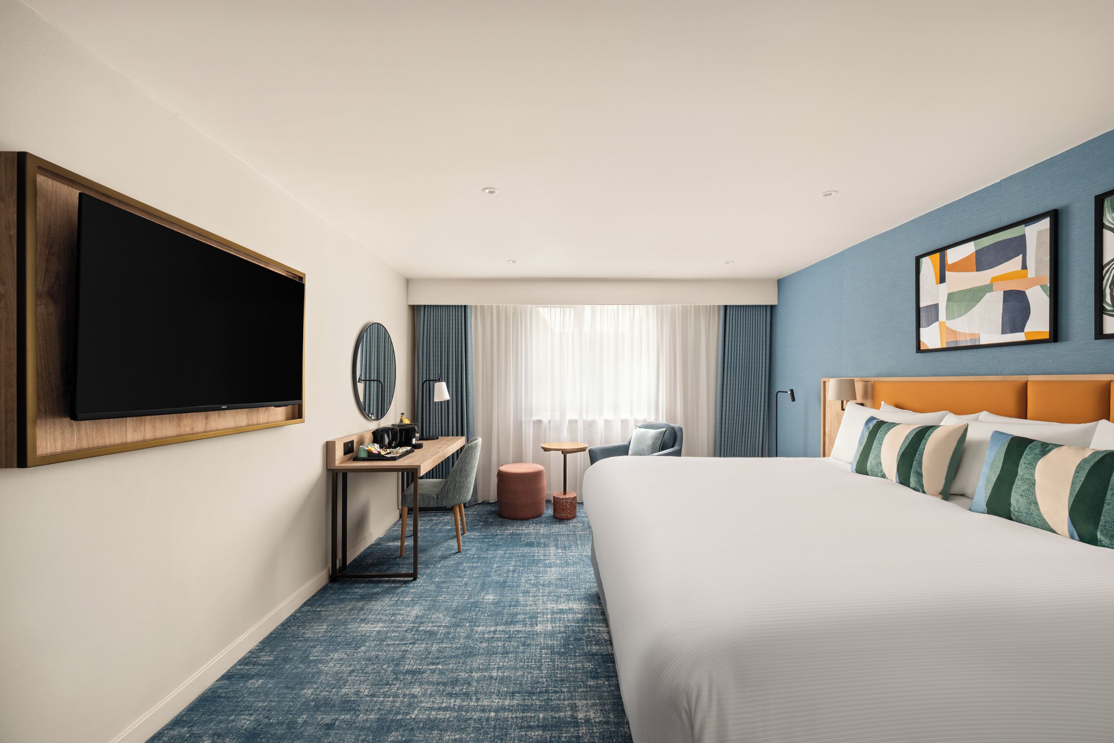 Habitación de hotel con una cama grande, un escritorio con silla, televisión y obras de arte en las paredes.