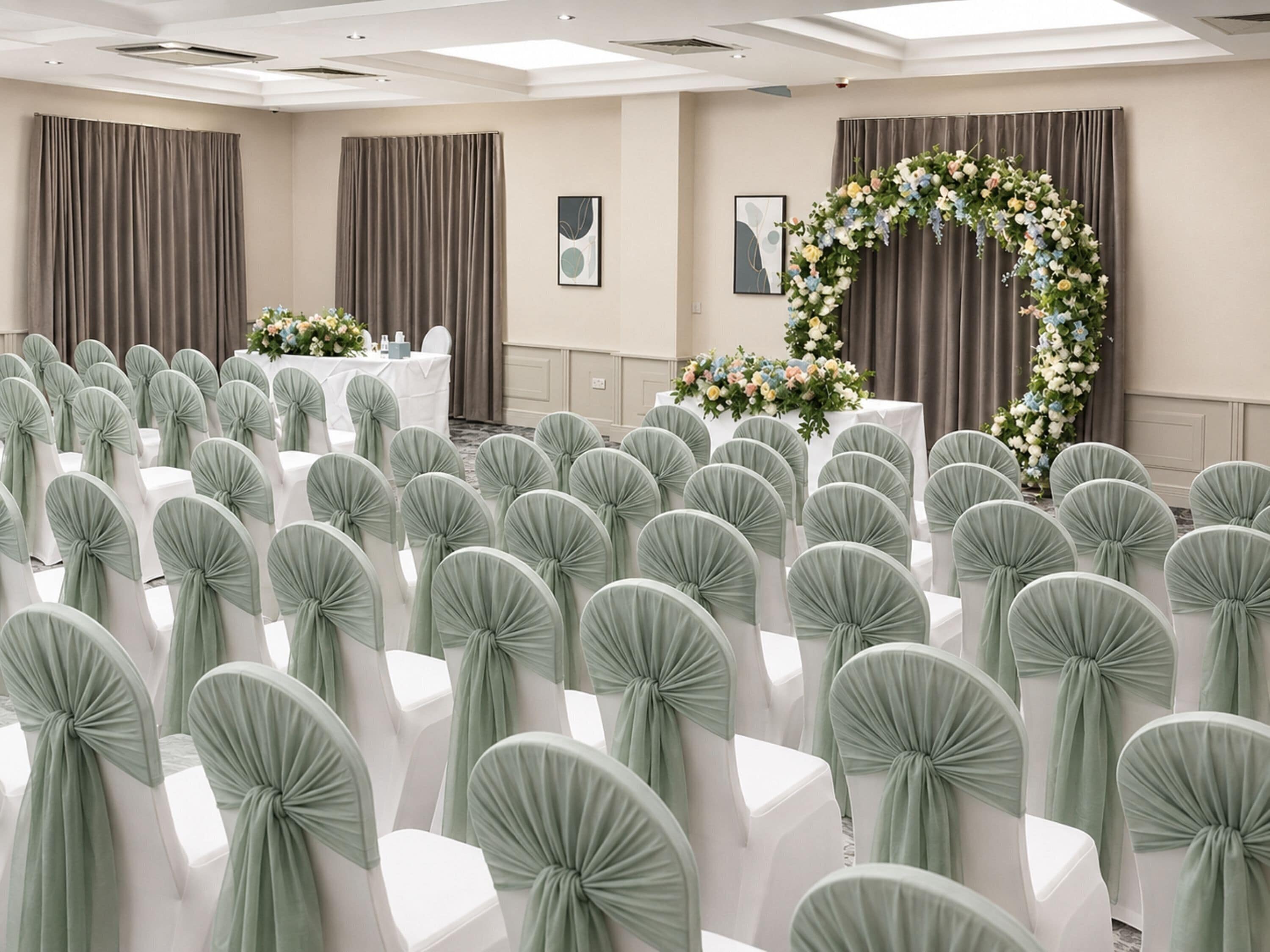 A conference room with rows of white chairs, grey curtains, and floral decorations.