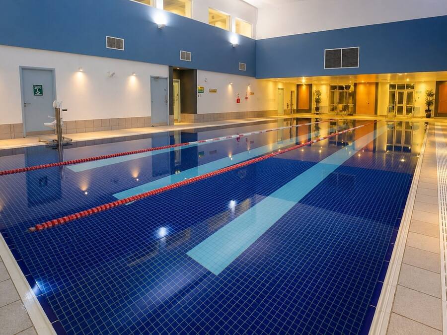 An indoor swimming pool with clear lanes, a blue tiled floor, and a reception area with a door and a sign.