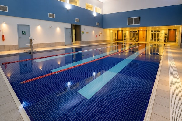 An indoor swimming pool with clear lanes, a blue tiled floor, and a reception area with a door and a sign.