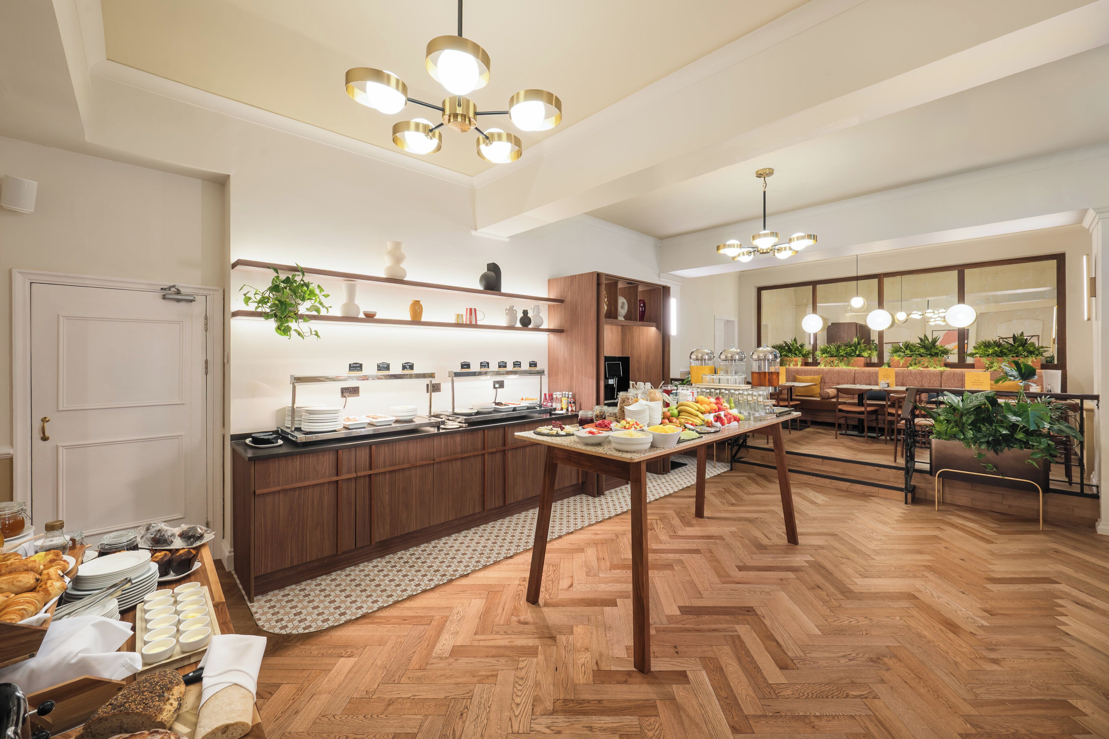 Eine moderne Hotelküche mit Holzschränken, einer Speiseauslage und einem Essbereich mit großem Spiegel und Pflanzen.