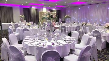 Une salle de banquet avec des tables rondes dressées pour un événement formel, comprenant des marque-places et une décoration de table soignée.