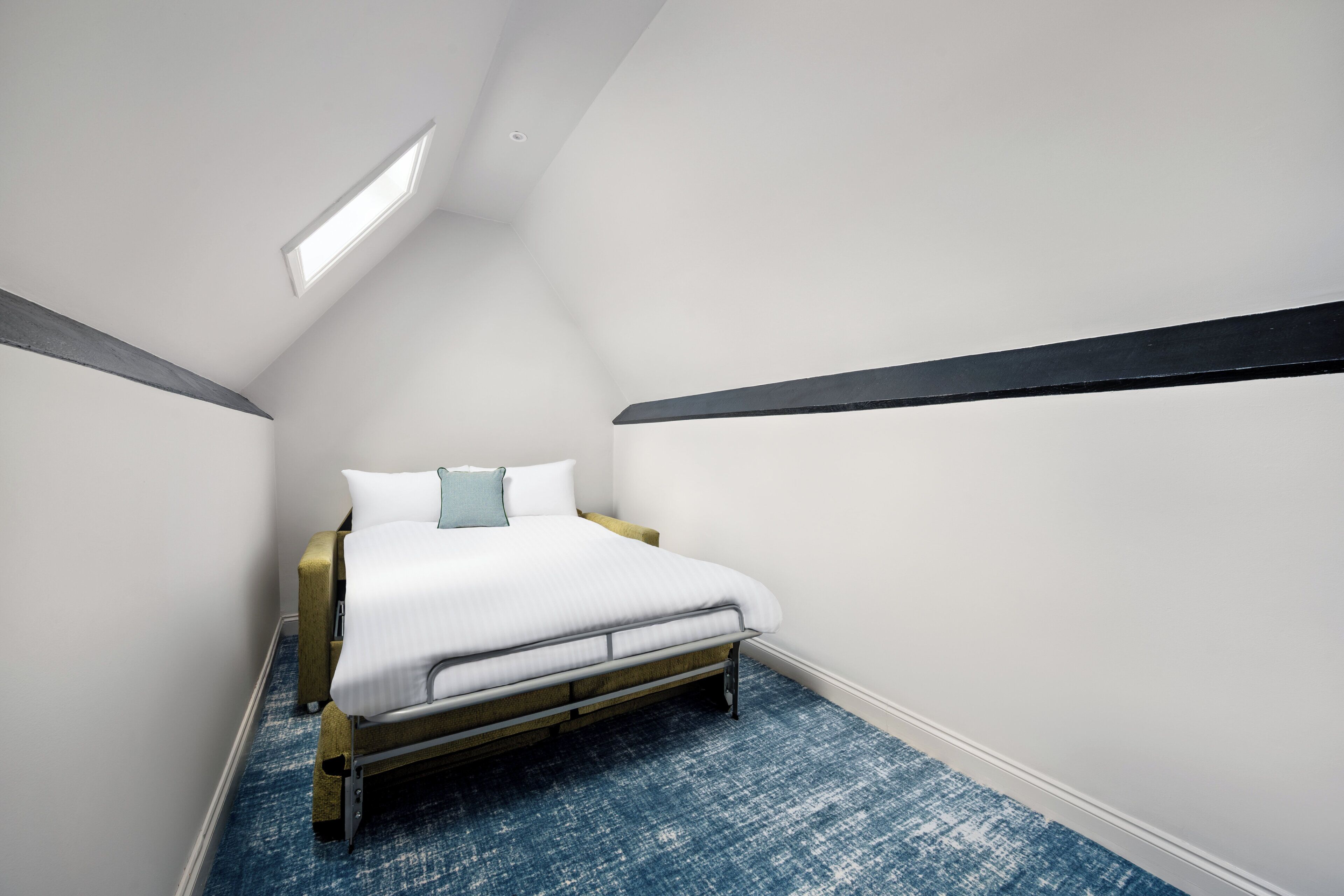 Un dormitorio con una cama, un tragaluz y una alfombra azul.