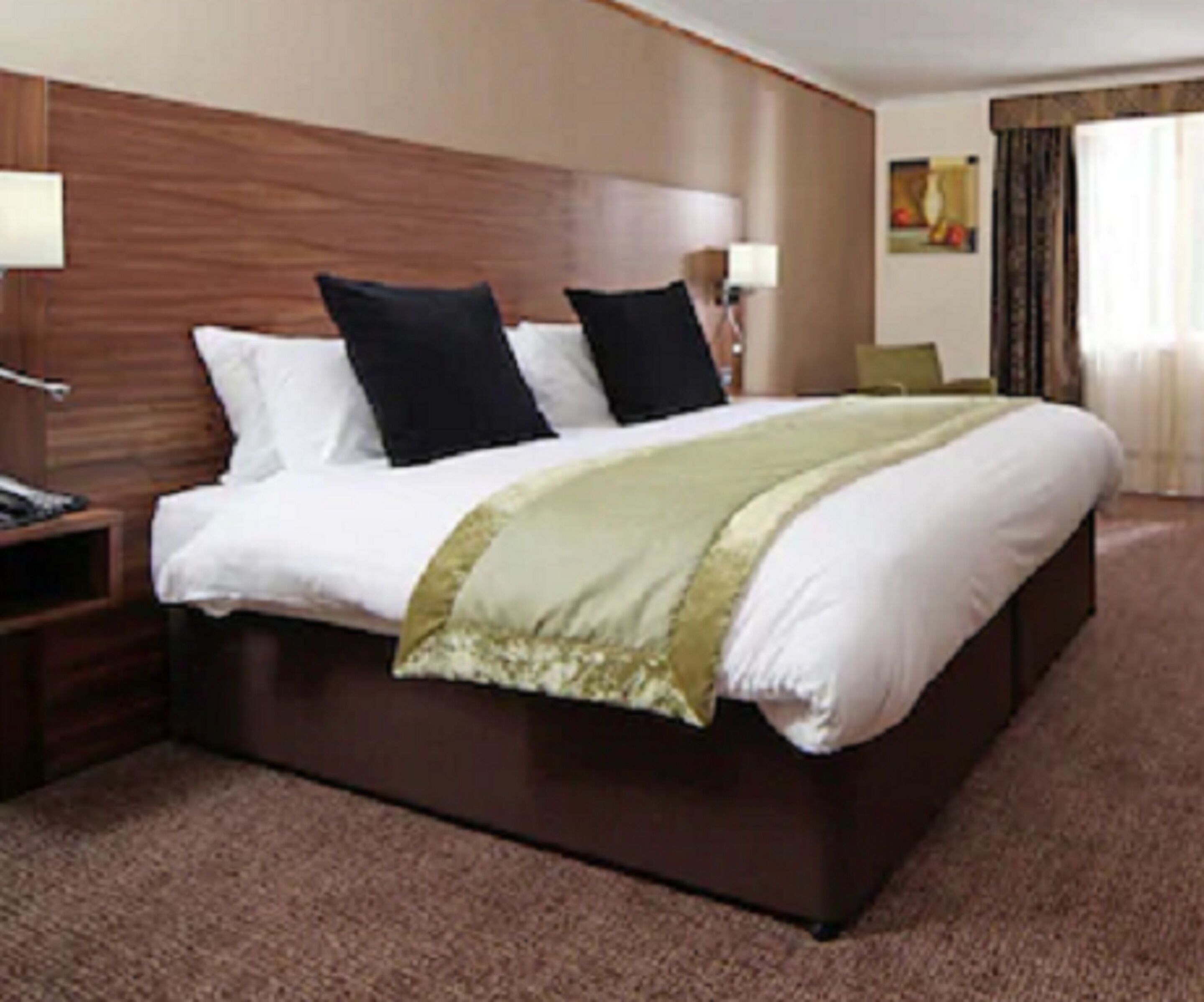 A hotel room with a large bed, wooden headboard, two bedside lamps, and a carpeted floor.