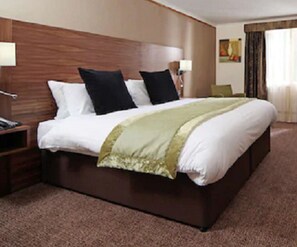 A hotel room with a large bed, wooden headboard, two bedside lamps, and a carpeted floor.