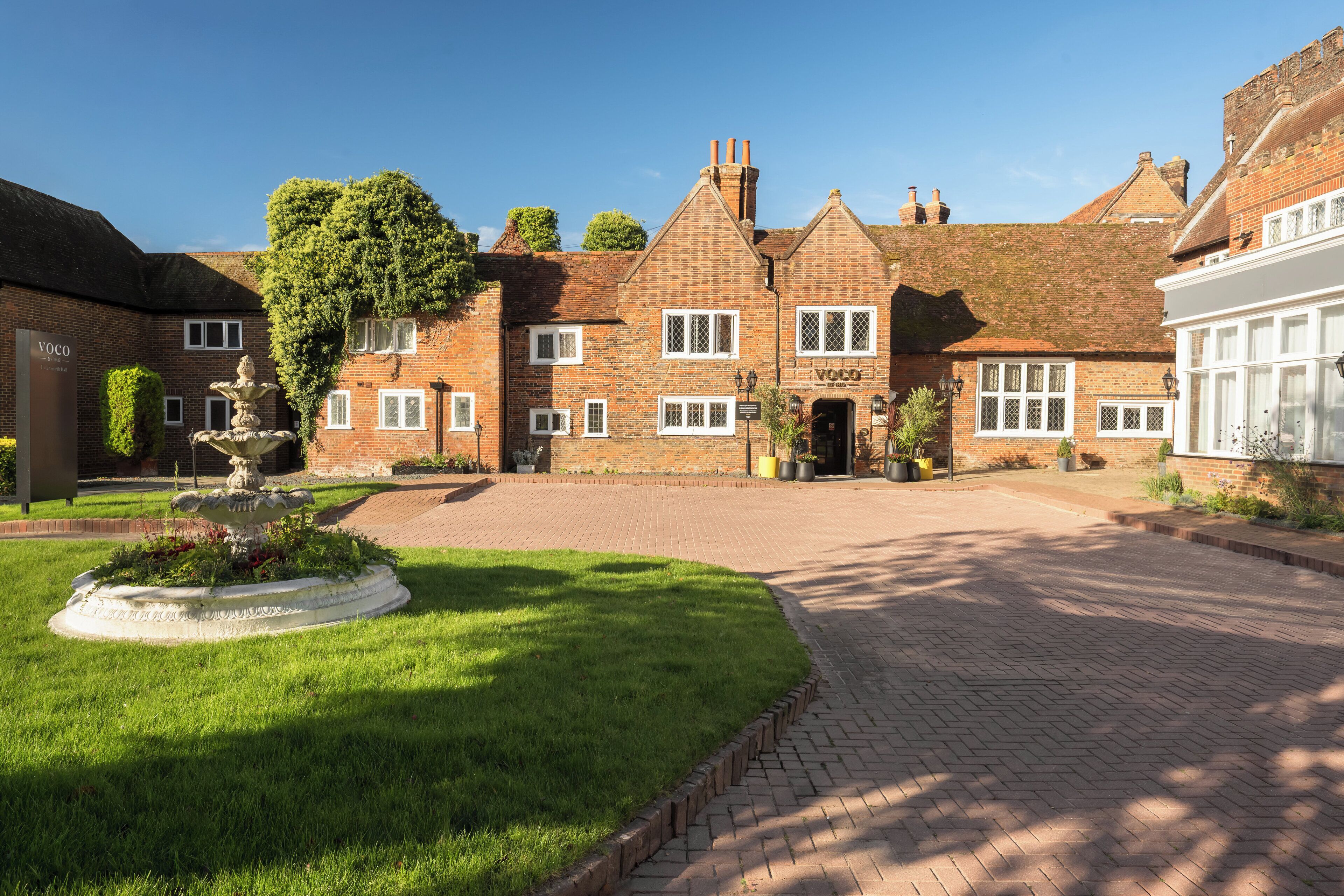 A traditional brick building with a central courtyard, a fountain, and a well-maintained lawn.